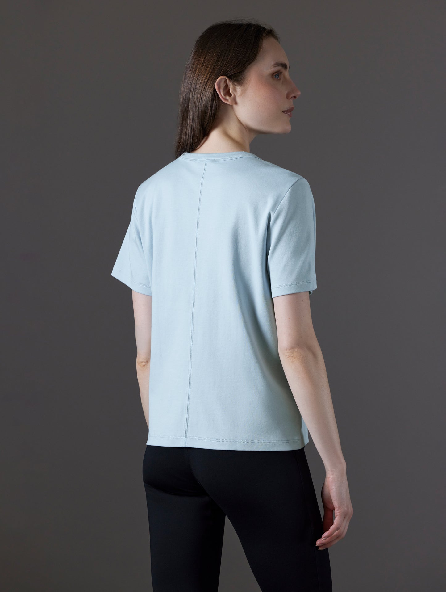 Rear angled view of woman wearing Emery Pima Tee in Flight Blue from AETHER Apparel.