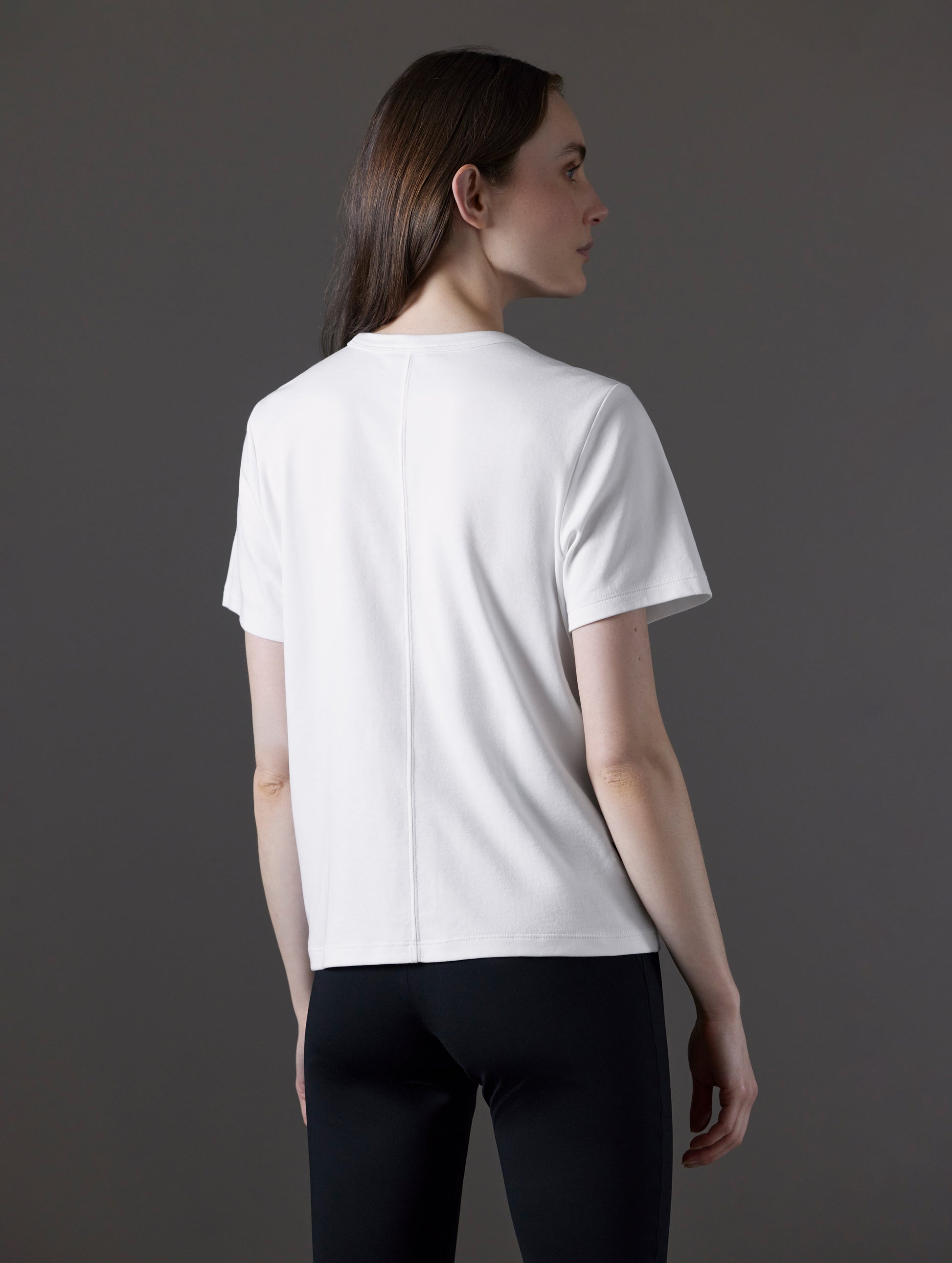 Rear angled view of woman wearing Emery Pima Tee in White from AETHER Apparel.