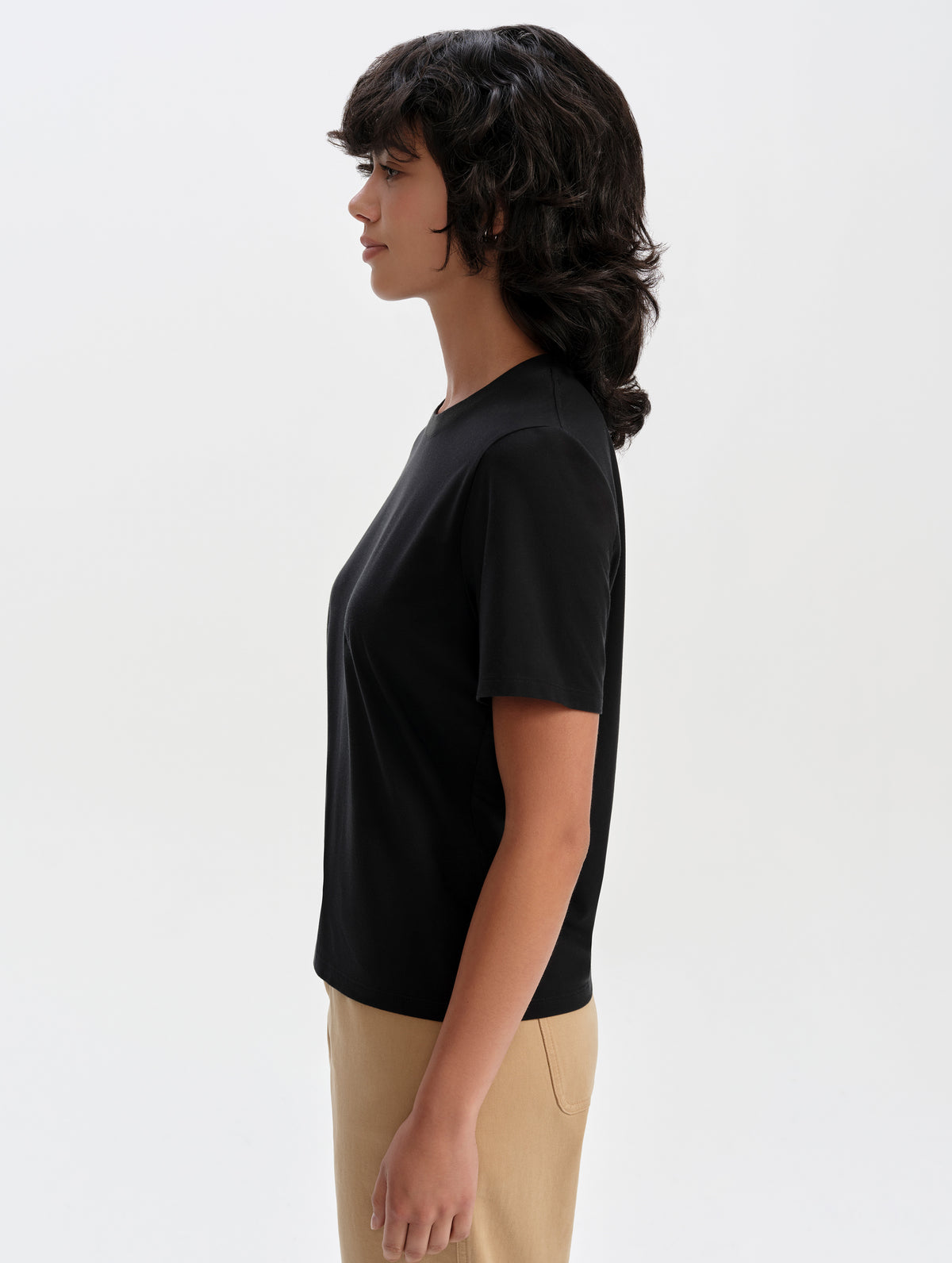 Side profile upper-body view of woman wearing the Hana Short-Sleeve Tee Shirt in Onyx Black from AETHER Apparel.