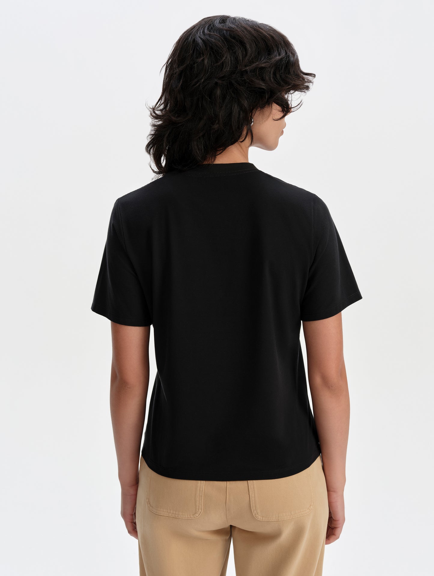 Rear upper-body view of woman wearing the Hana Short-Sleeve Tee Shirt in Onyx Black from AETHER Apparel.
