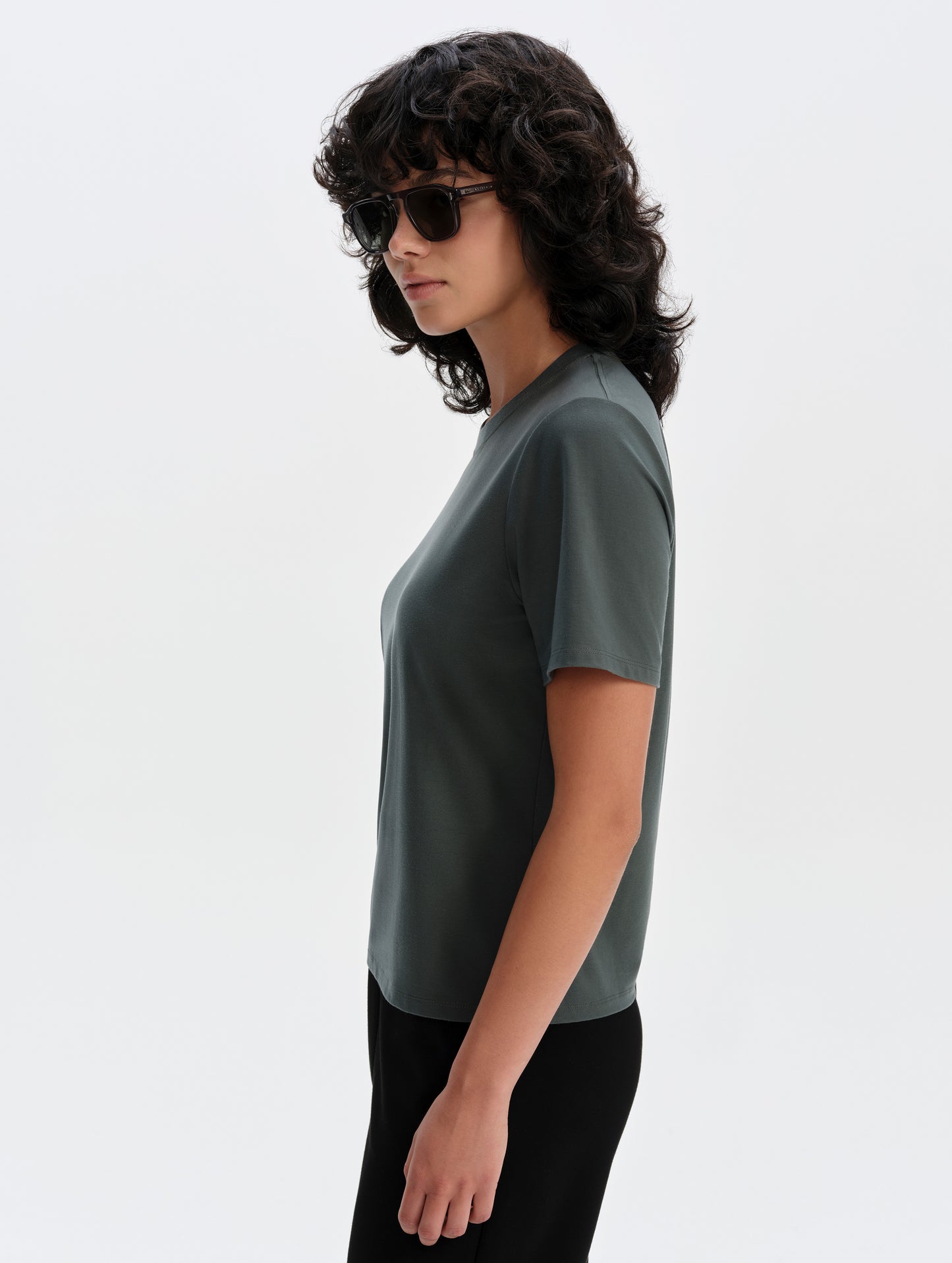 Side profile upper-body view of woman wearing the Hana Short-Sleeve Tee Shirt in Saville Green from AETHER Apparel.