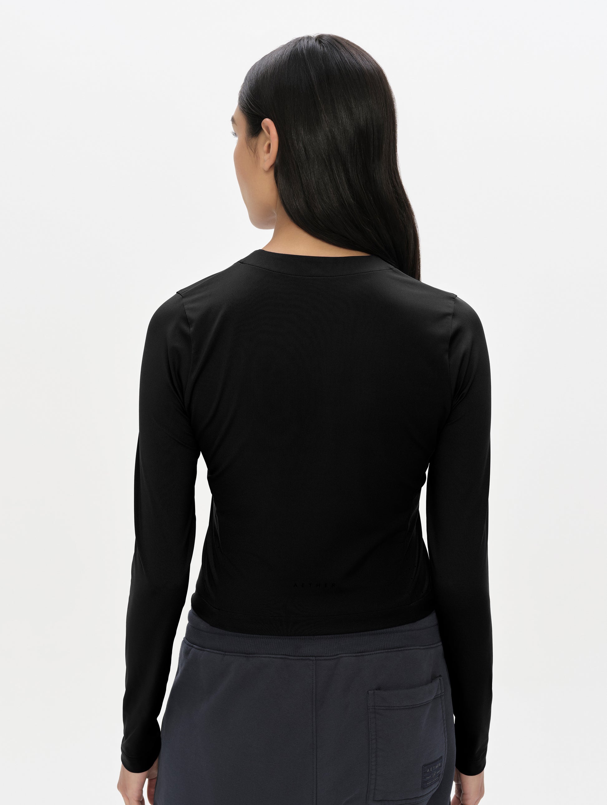 Rear, upper-body view of woman wearing the Kora Sunproof Shirt in Onyx Black from AETHER Apparel.
