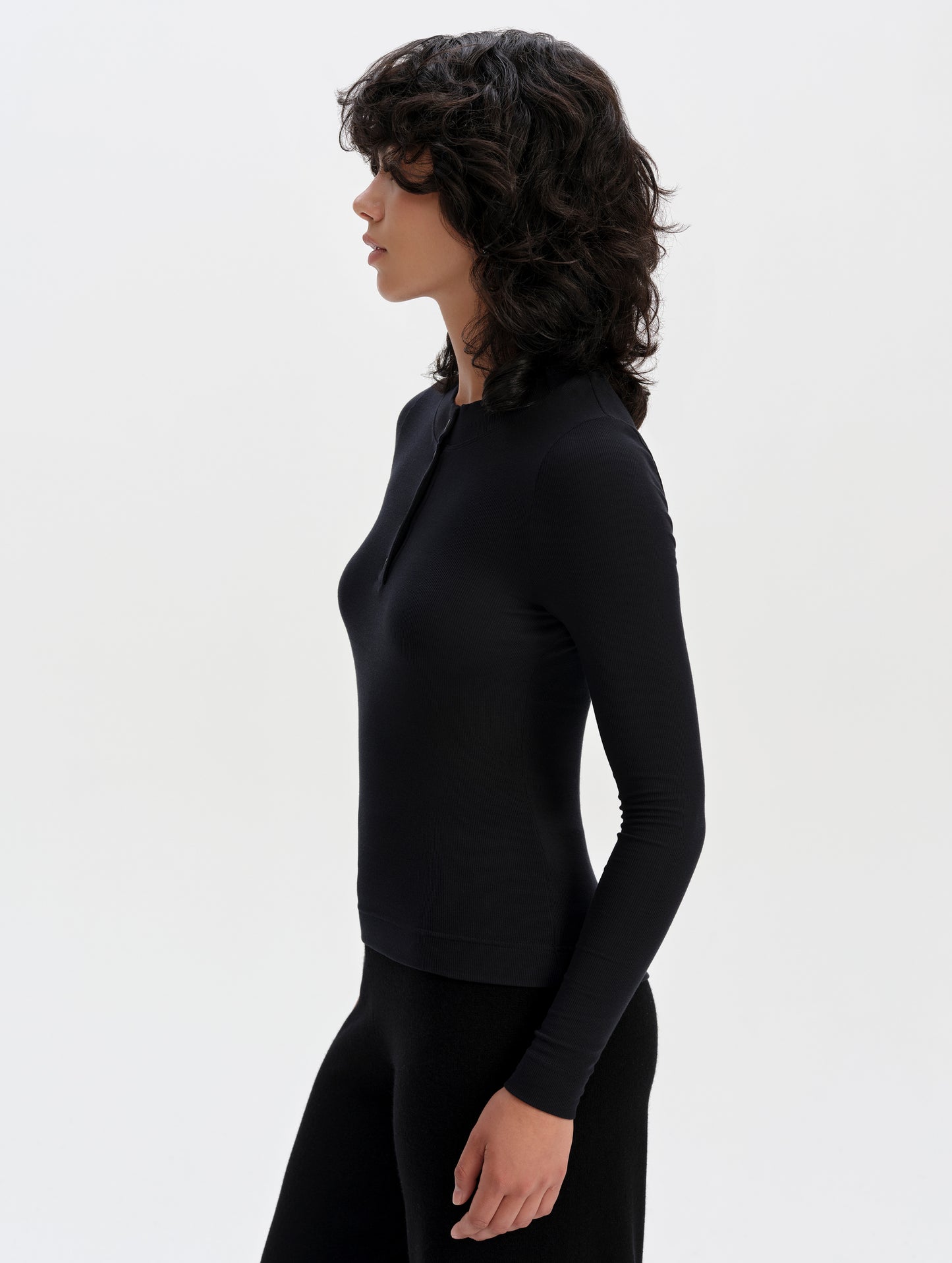Side profile upper-body view of woman wearing the Legacy Long-Sleeve Henley in Onyx Black from AETHER Apparel.