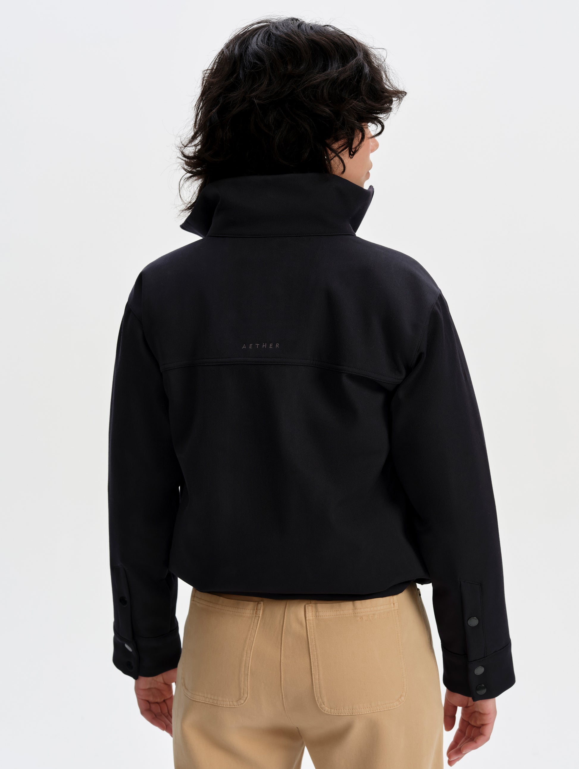 Rear upper-body view of woman wearing the Luna 3-in-1 Field Jacket in Onyx Black from AETHER Apparel.