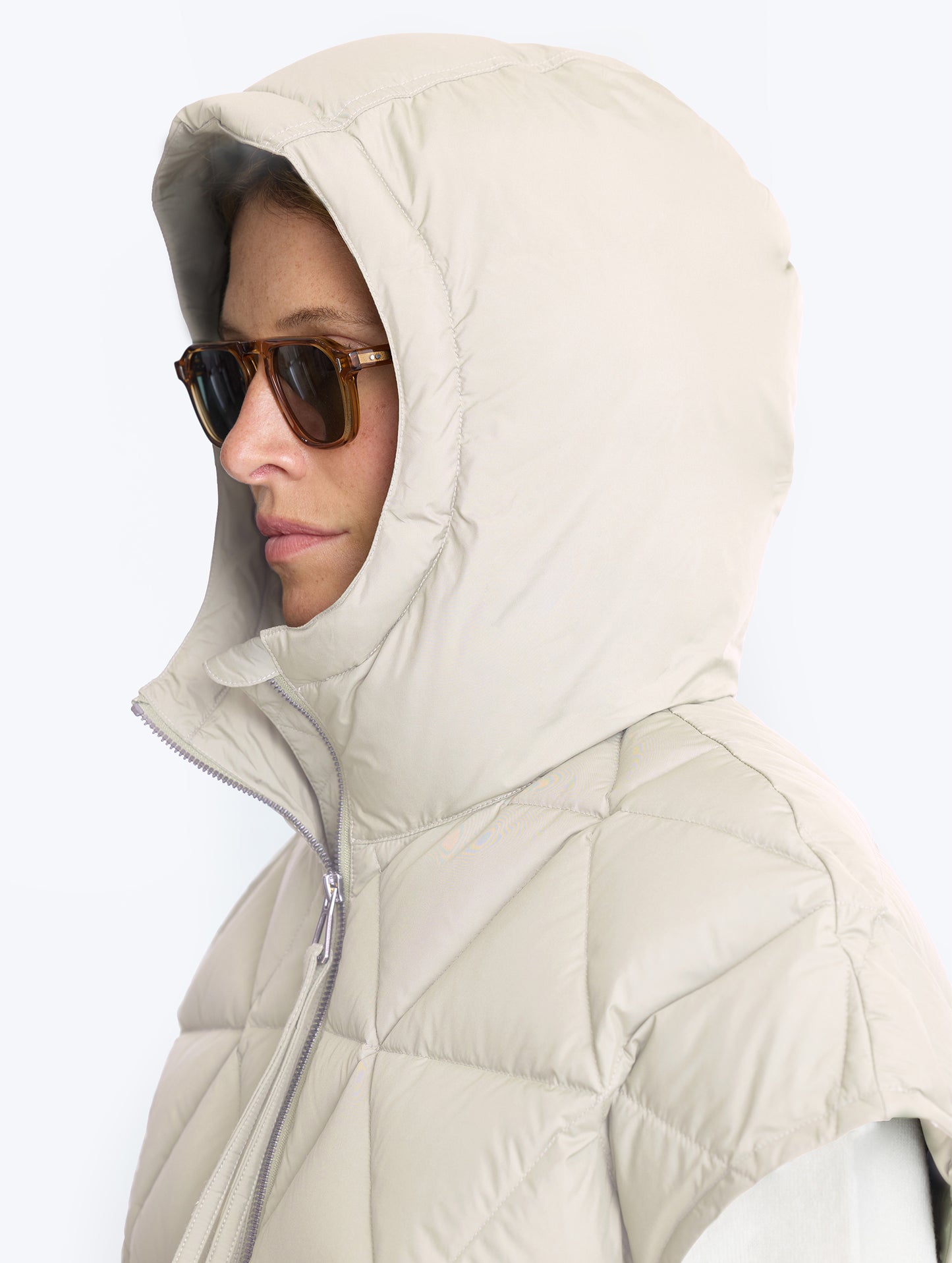 Closeup view of woman wearing hood of Mailen Oversized Vest in Bone White from AETHER Apparel.