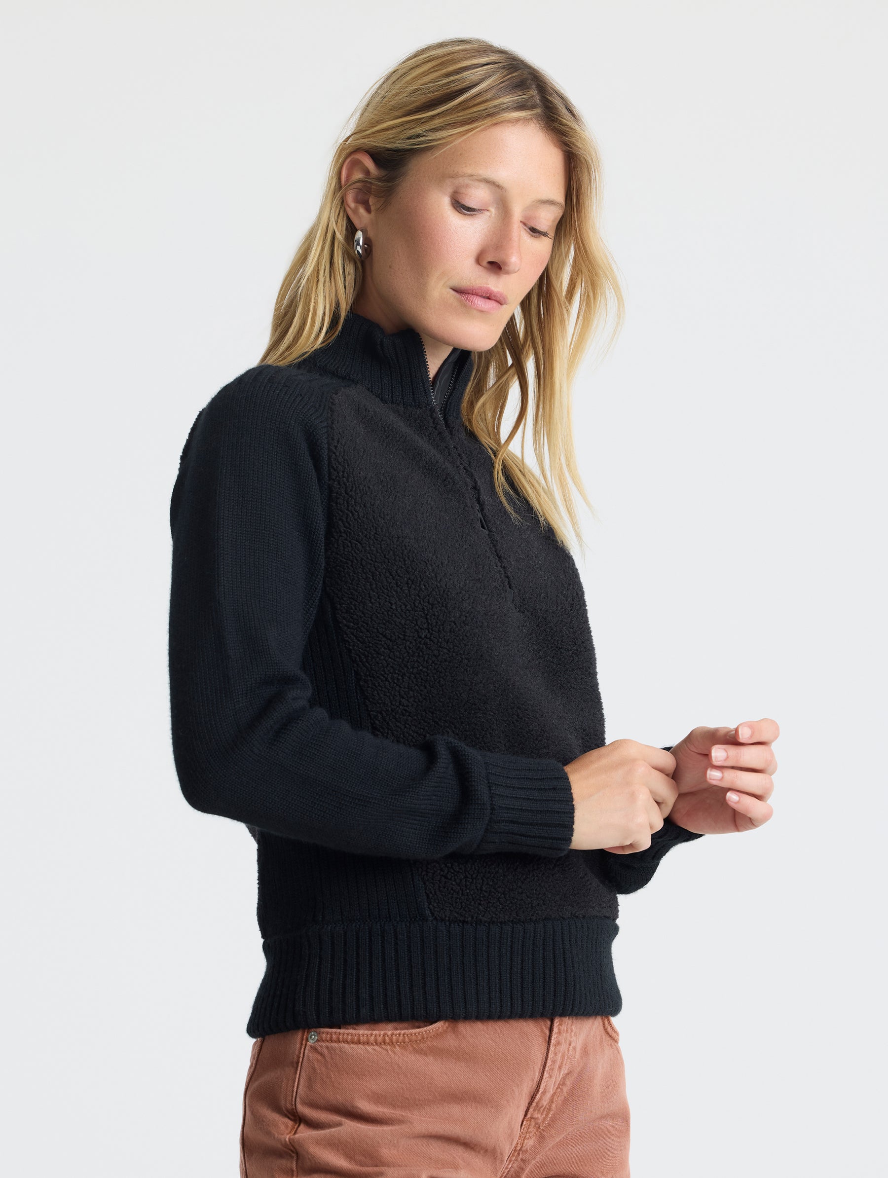 Front angled view of woman holding left sleeve wearing Malina Half-Zip Sweater in Onyx Black from AETHER Apparel.