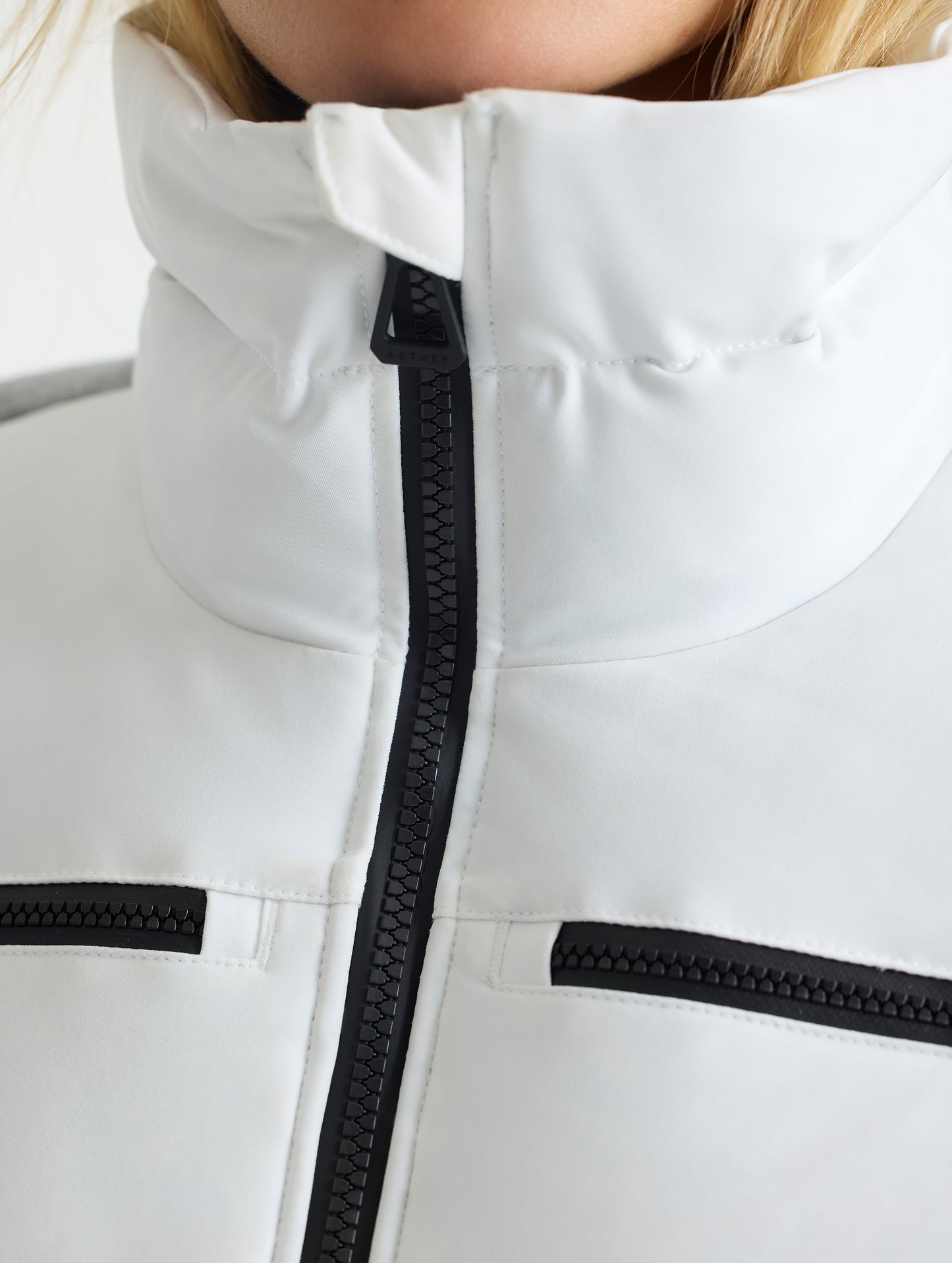 Closeup detailed view of the main center-front zipper closure and collar on the Nordic Jacket 2.0 in Winter White from AETHER Apparel.