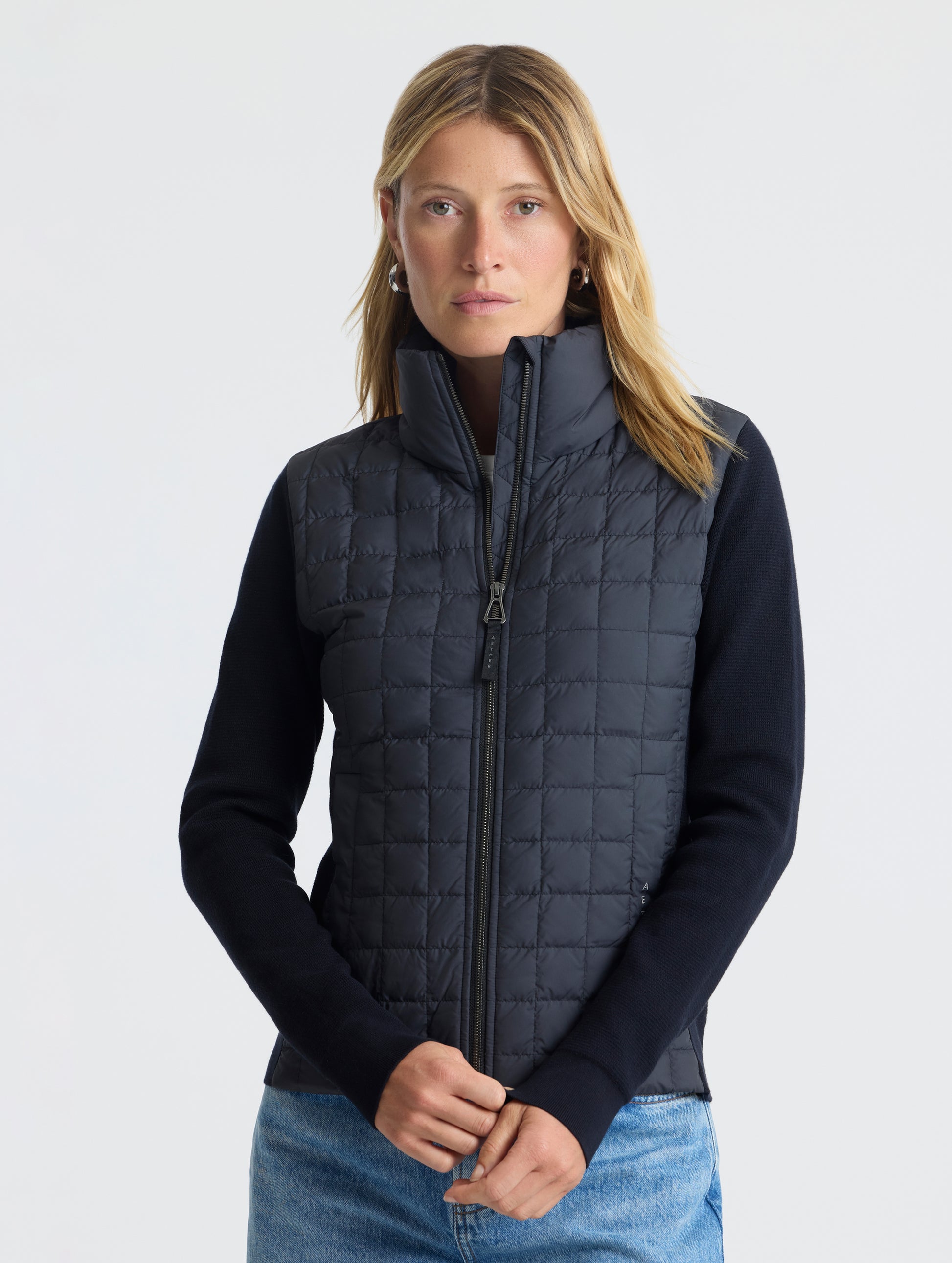 Front, upper-body view of woman wearing zipped-up Phase Full-Zip in Onyx Black from AETHER Apparel.