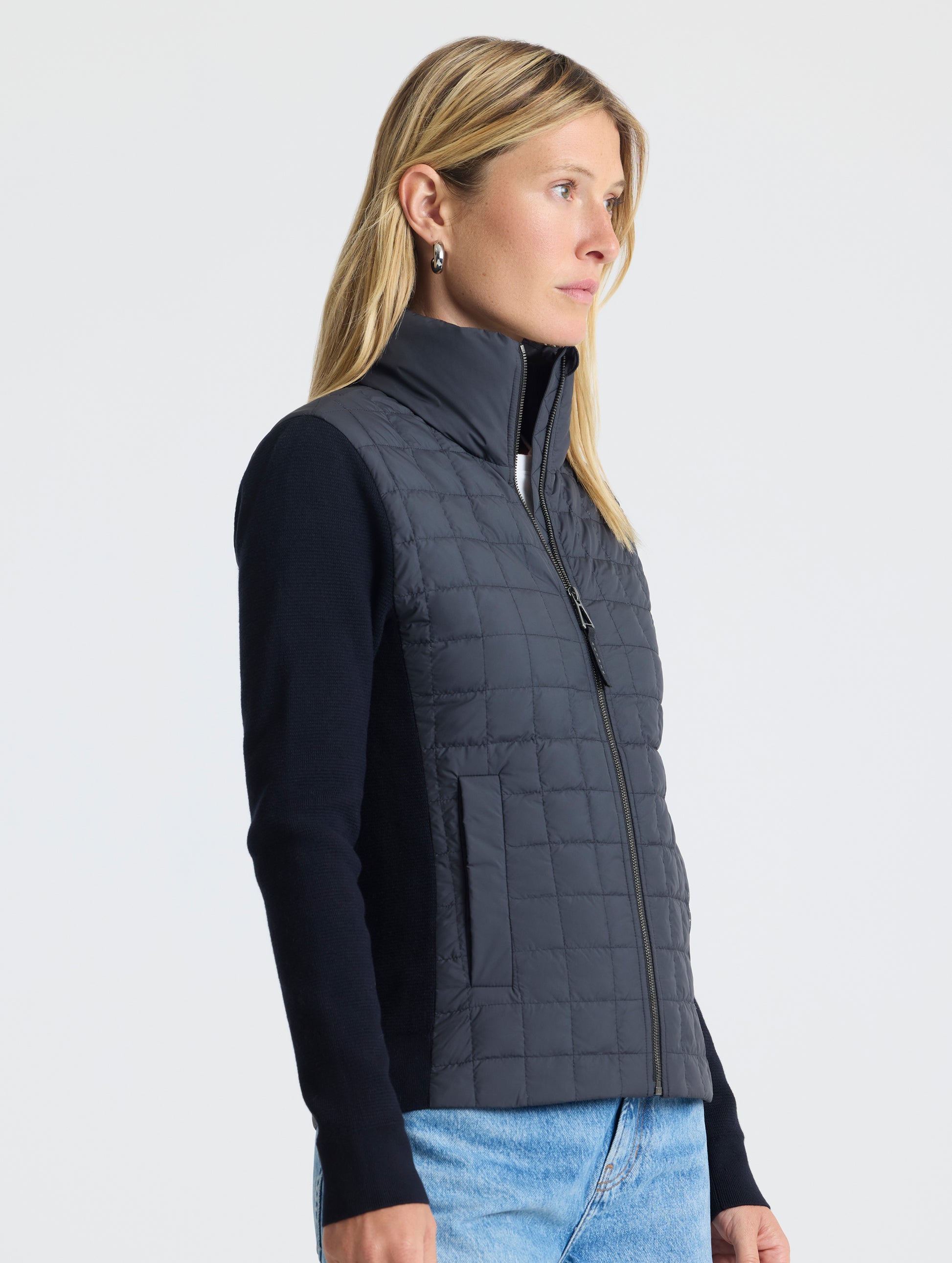 Front, angled, upper-body view of woman wearing zipped-up Phase Full-Zip in Onyx Black from AETHER Apparel.
