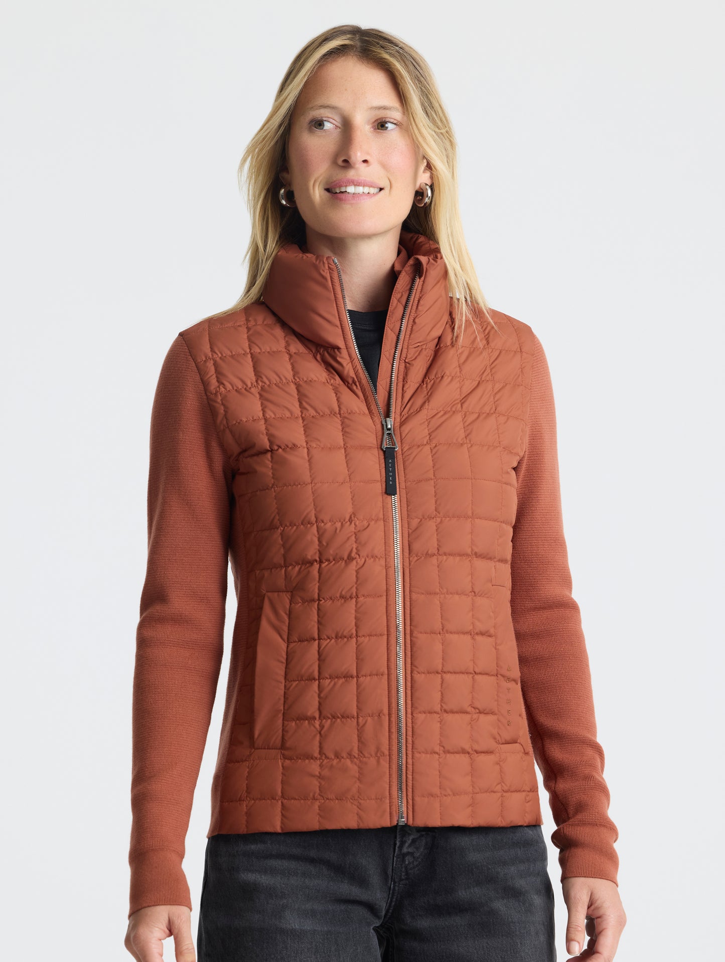 Front, upper-body view of woman wearing zipped-up Phase Full-Zip in Redwood Rust from AETHER Apparel.
