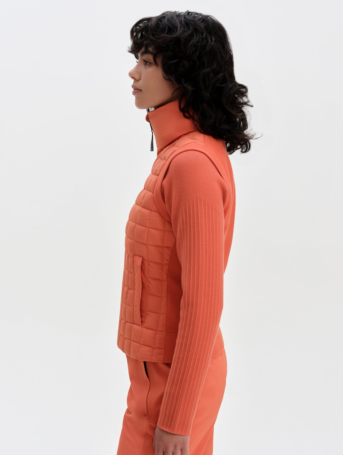 Side profile upper-body view of woman wearing the Phase Vest in Madeira Orange from AETHER Apparel.