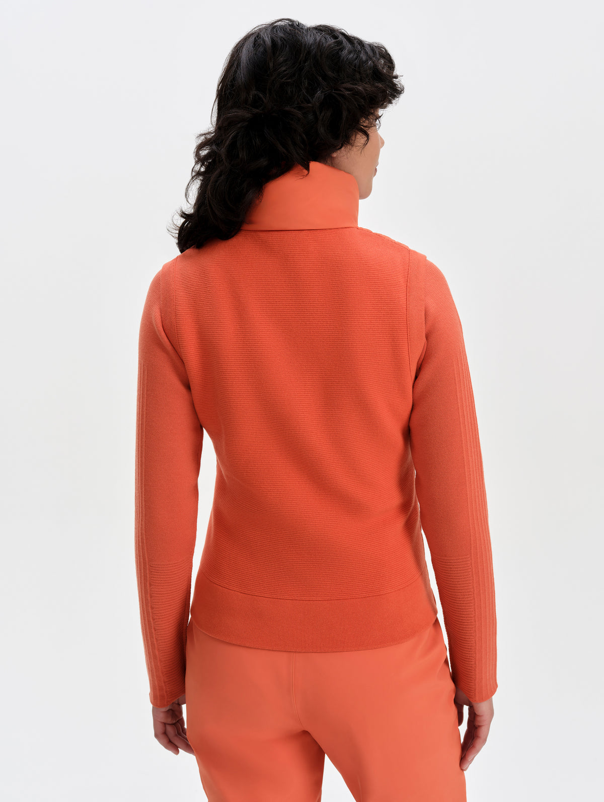 Rear upper-body view of woman wearing the Phase Vest in Madeira Orange from AETHER Apparel.