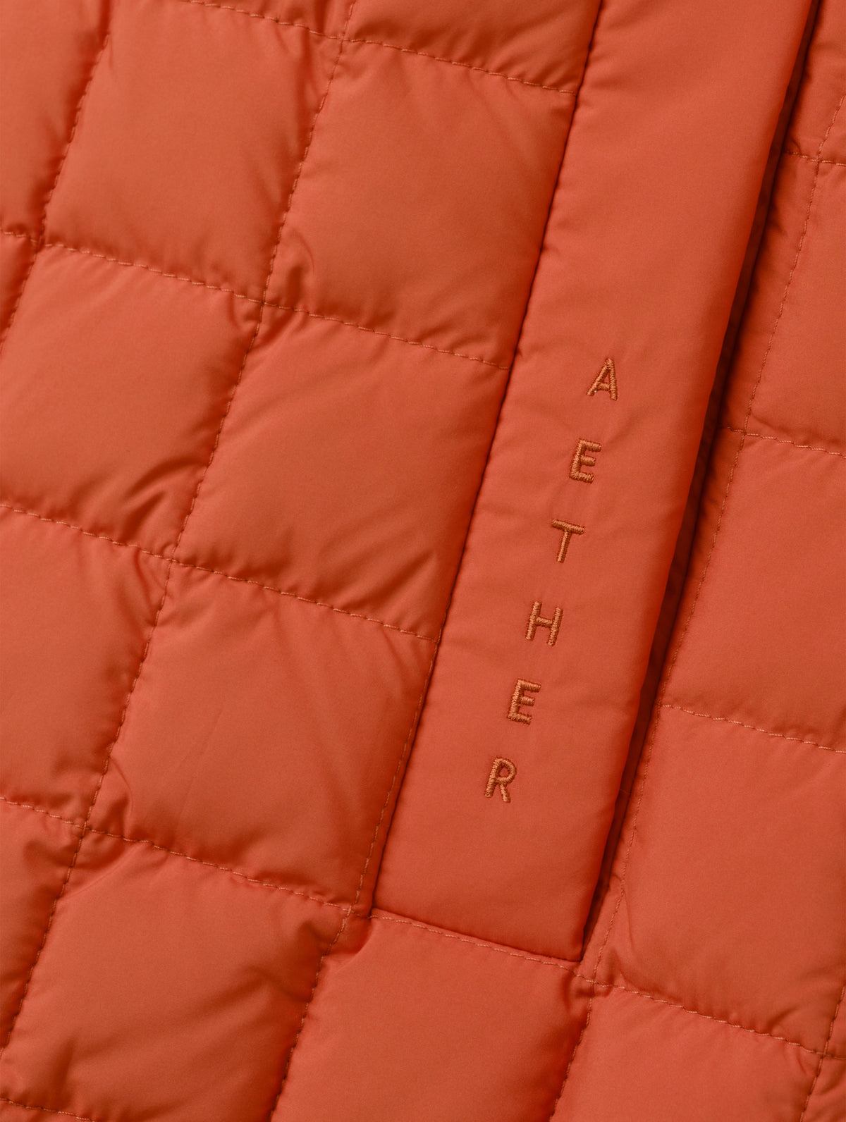 Closeup detailed view of the embroidered wordmark and box quilting on the Phase Vest in Madeira Orange from AETHER Apparel.