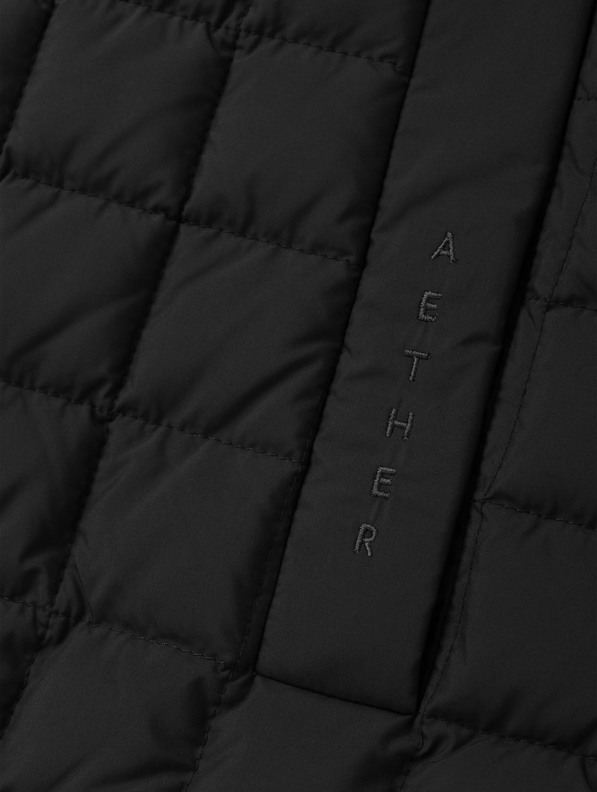 Closeup detailed view of the embroidered wordmark and box quilting on the Phase Vest in Onyx Black from AETHER Apparel.