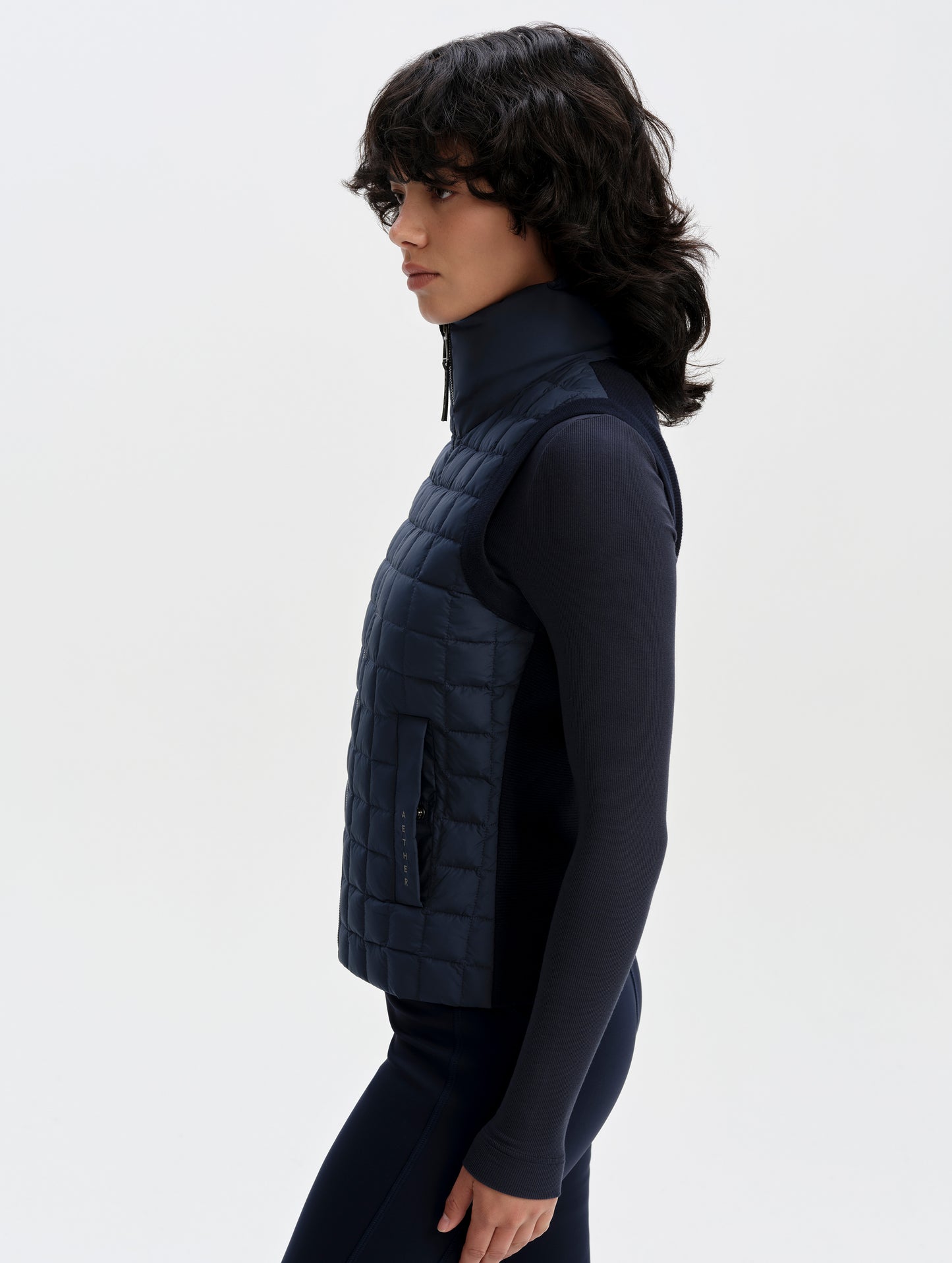 Side profile upper-body view of woman wearing the Phase Vest in Total Eclipse from AETHER Apparel.