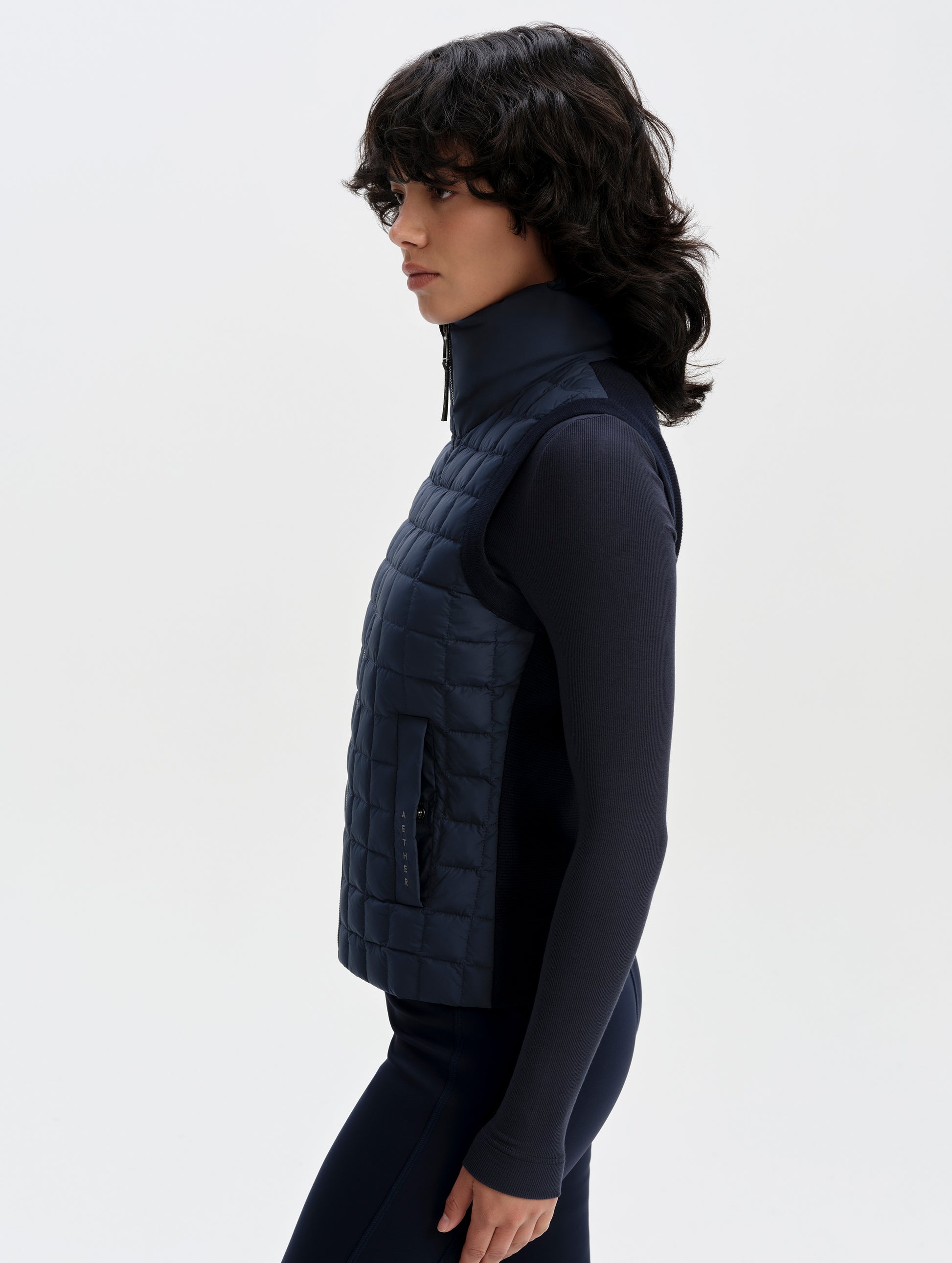 Side profile upper-body view of woman wearing the Phase Vest in Total Eclipse from AETHER Apparel.