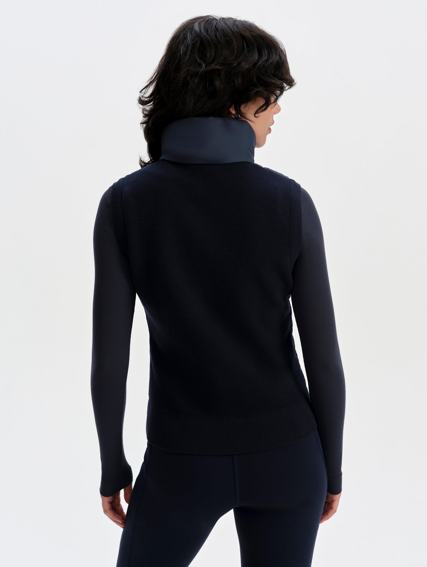 Rear upper-body view of woman wearing the Phase Vest in Total Eclipse from AETHER Apparel.
