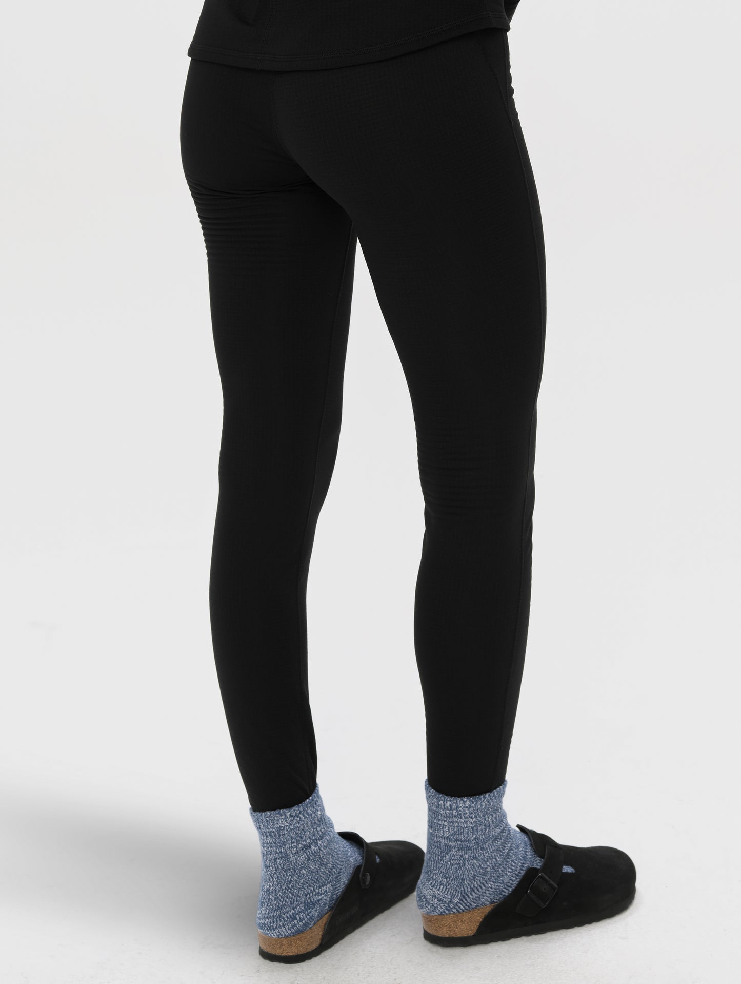 Rear angled lower-body view of woman wearing Polar Base Layer Pant in Onyx Black from AETHER Apparel.