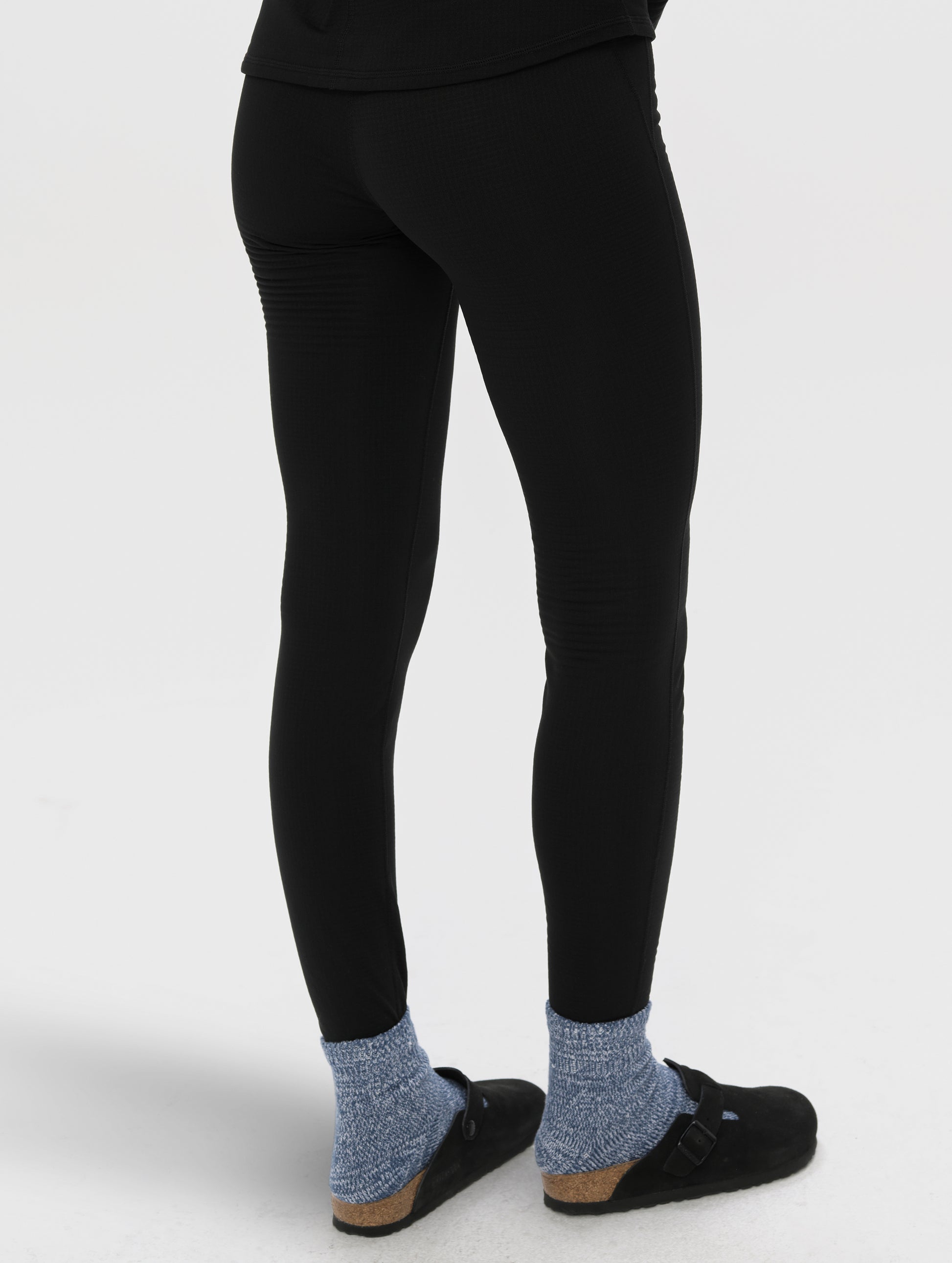 Rear angled lower-body view of woman wearing Polar Base Layer Pant in Onyx Black from AETHER Apparel.