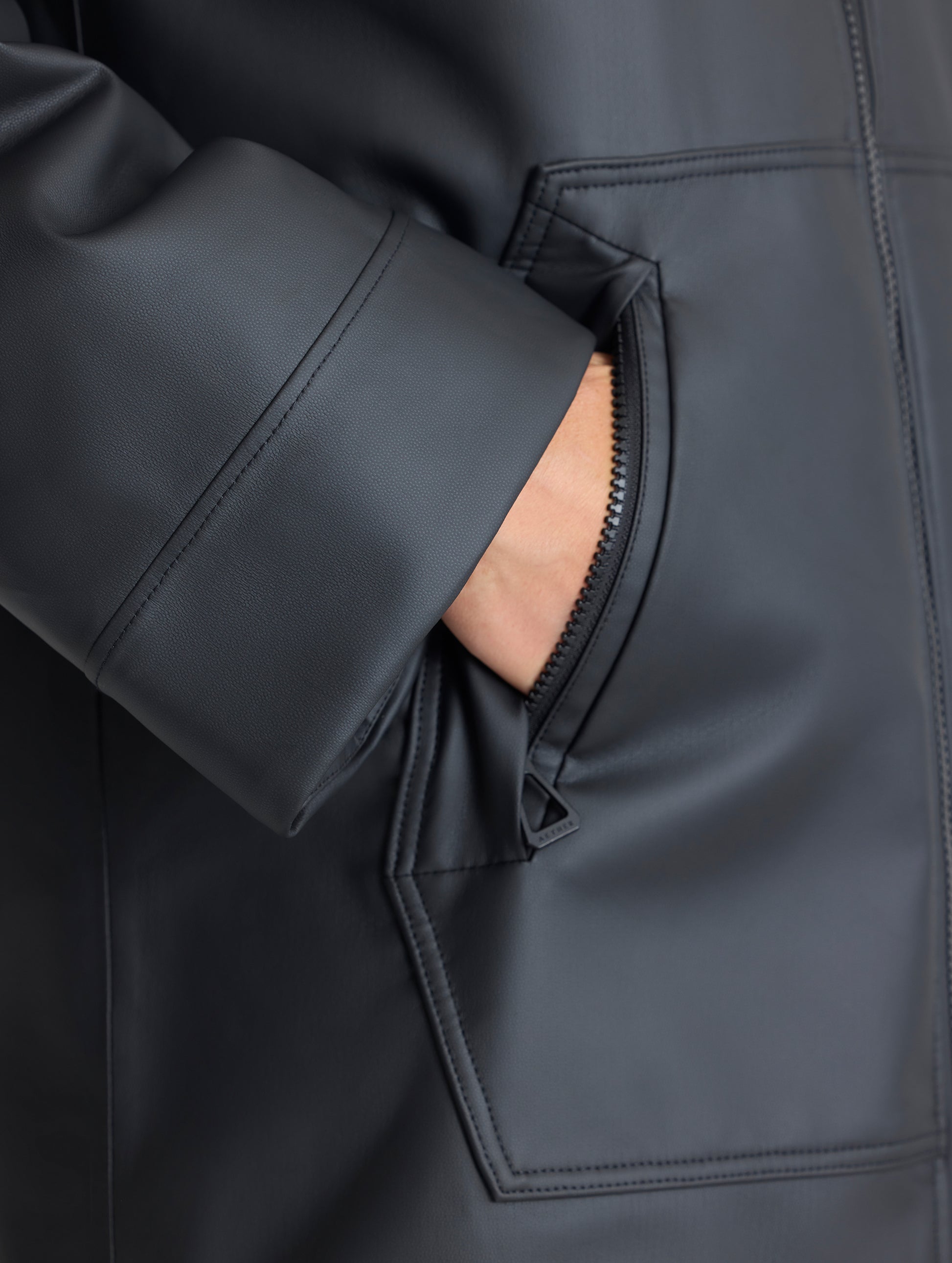 Closeup detailed view of woman placing hand into pocket of the Quest Sherpa-Lined Rain Jacket Onyx Black from AETHER Apparel. 