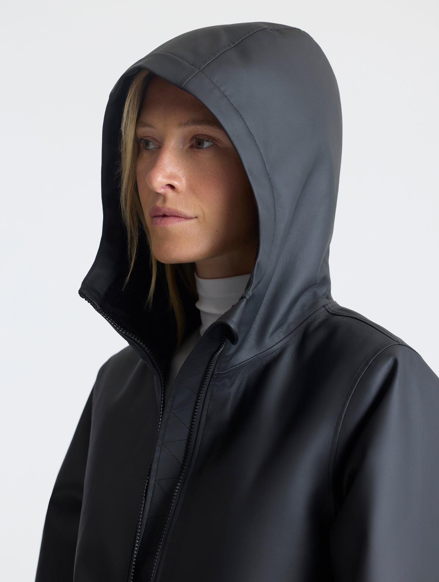 Front angled upper-body view of woman with hood up wearing the Quest Sherpa-Lined Rain Jacket Onyx Black from AETHER Apparel. 