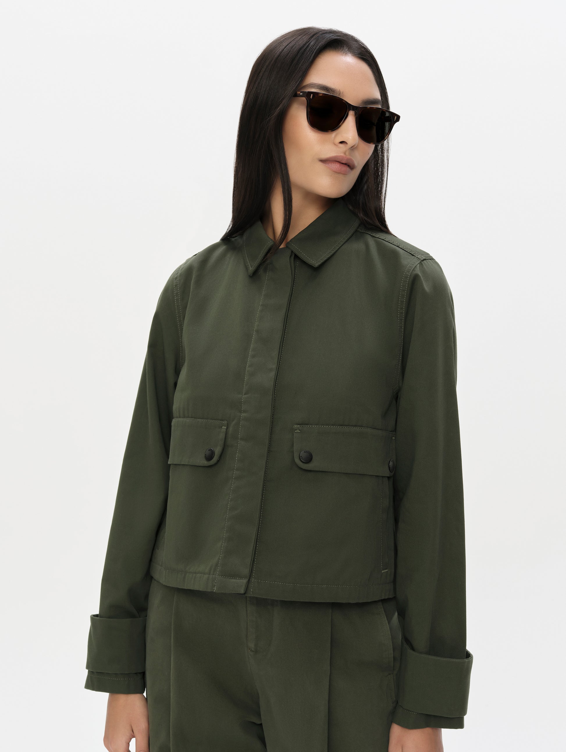 Front, upper-body view of woman wearing the Raven Waxed Cotton Jacket in Forest Green from AETHER Apparel.