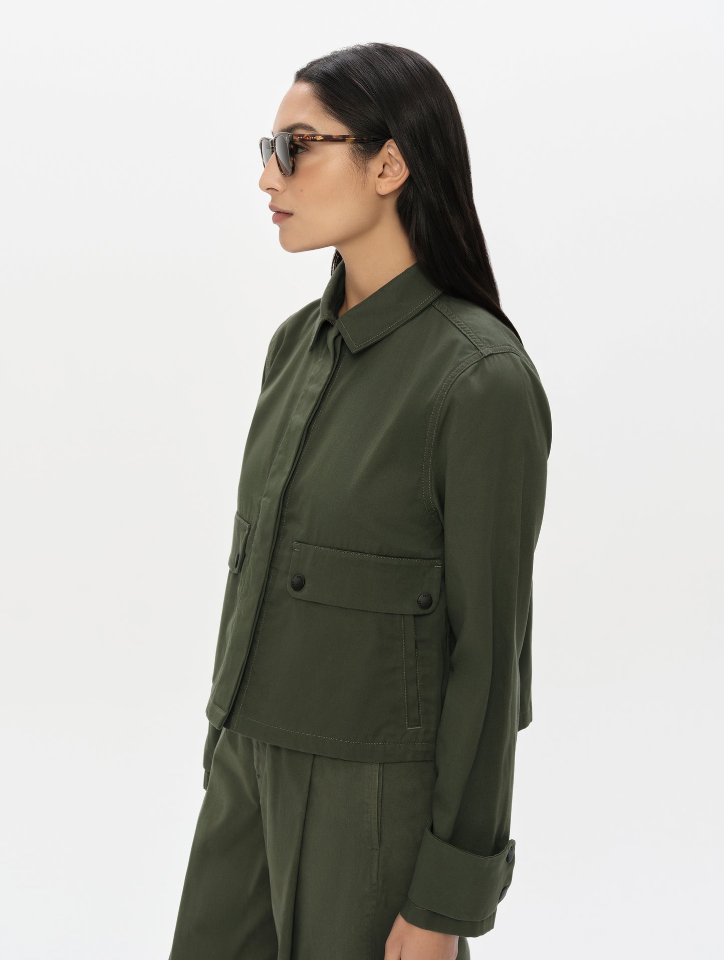 Side profile, upper-body view of woman wearing the Raven Waxed Cotton Jacket in Forest Green from AETHER Apparel.