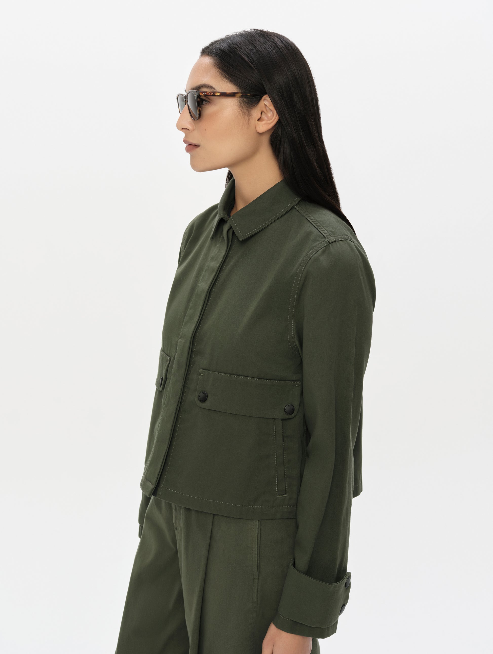 Side profile, upper-body view of woman wearing the Raven Waxed Cotton Jacket in Forest Green from AETHER Apparel.