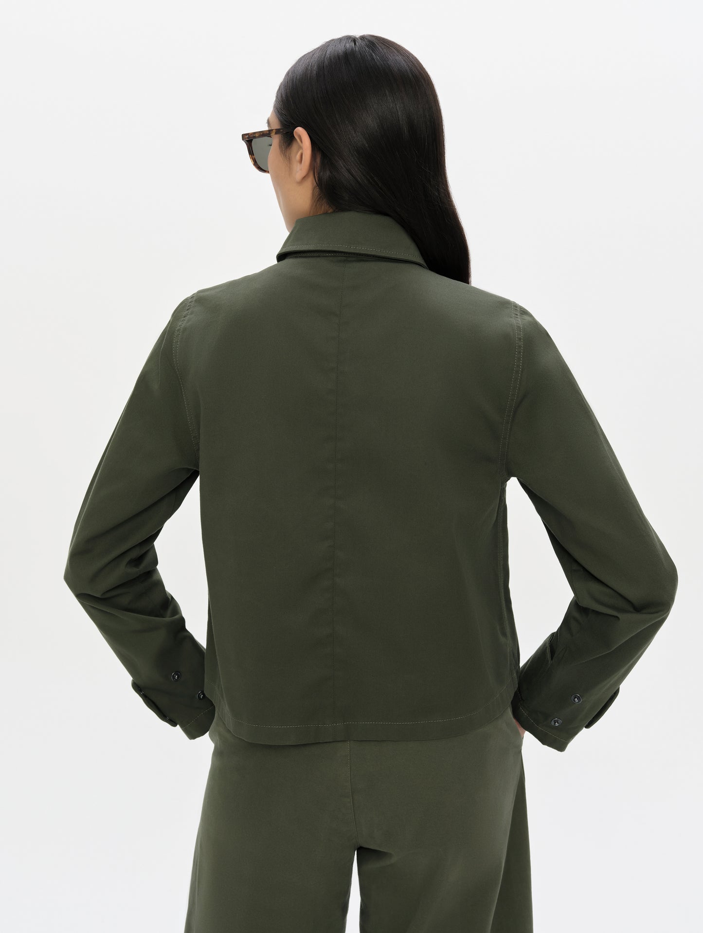 Rear, upper-body view of woman wearing the Raven Waxed Cotton Jacket in Forest Green from AETHER Apparel.
