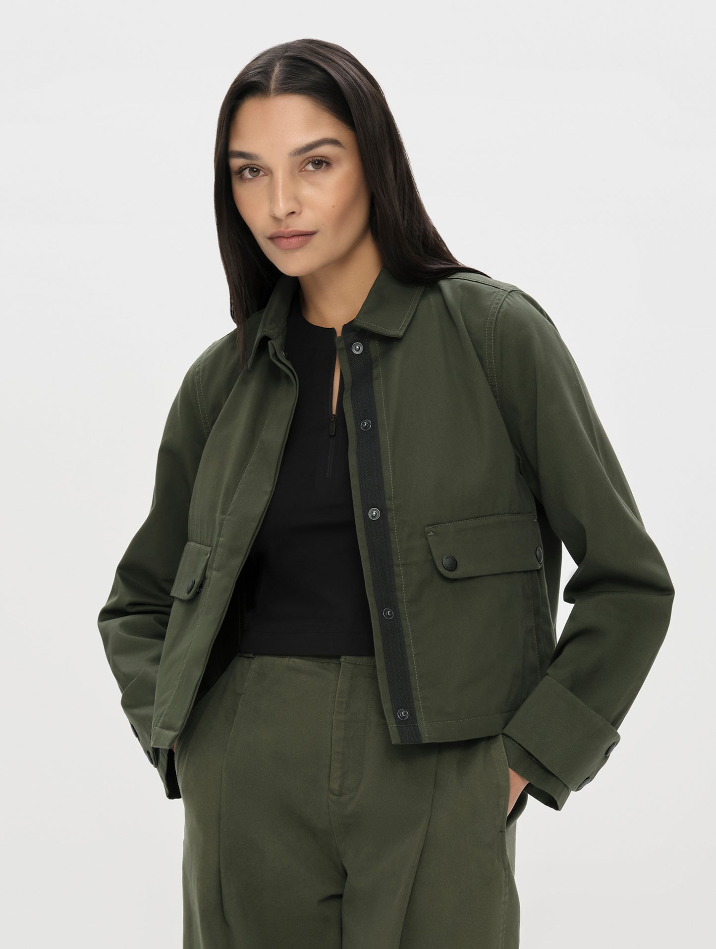 Front, upper-body view of woman wearing the Raven Waxed Cotton Jacket in Forest Green from AETHER Apparel unsnapped. 