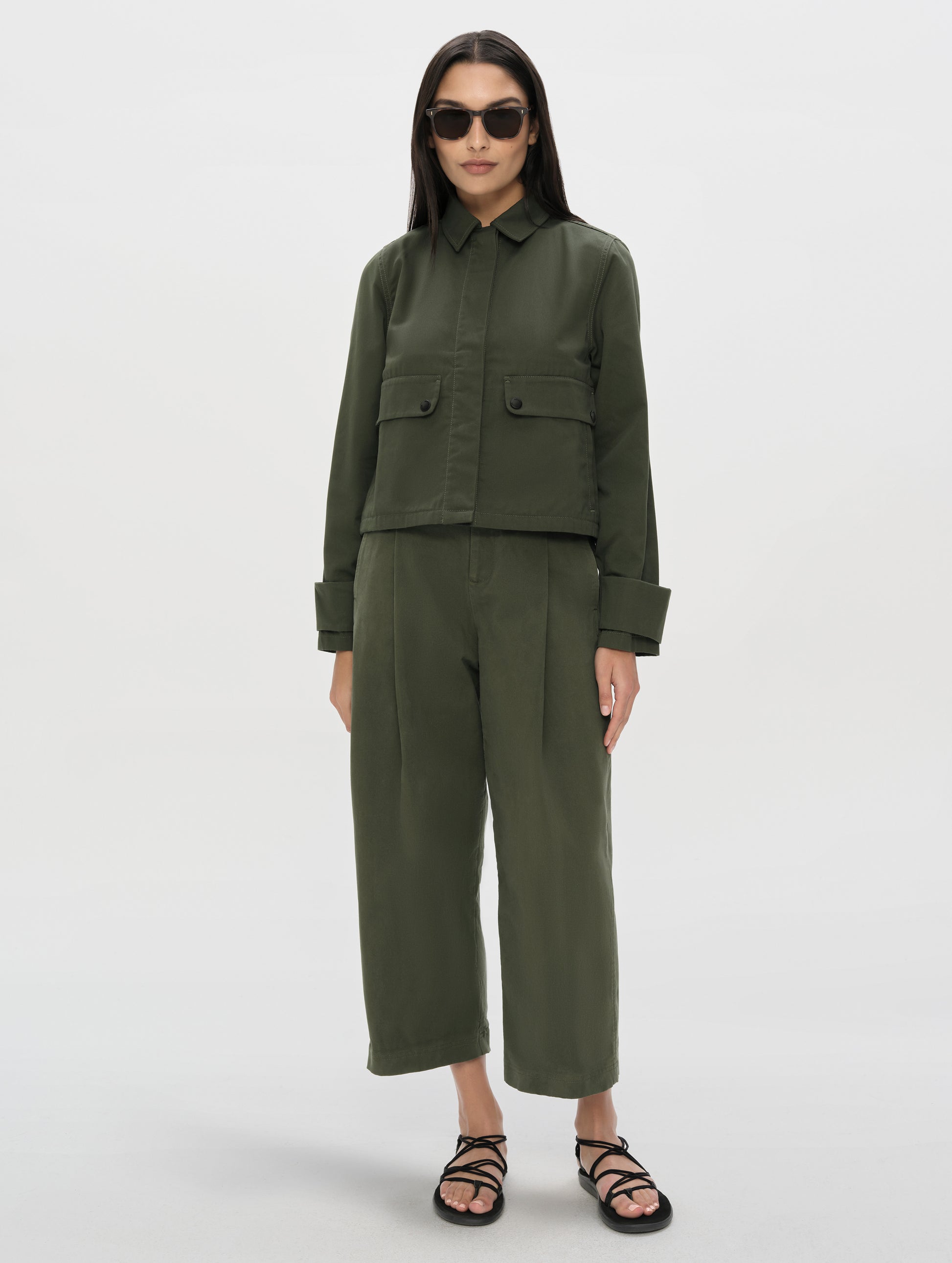 Front, full-body view of woman wearing the Raven Waxed Cotton Jacket in Forest Green from AETHER Apparel.