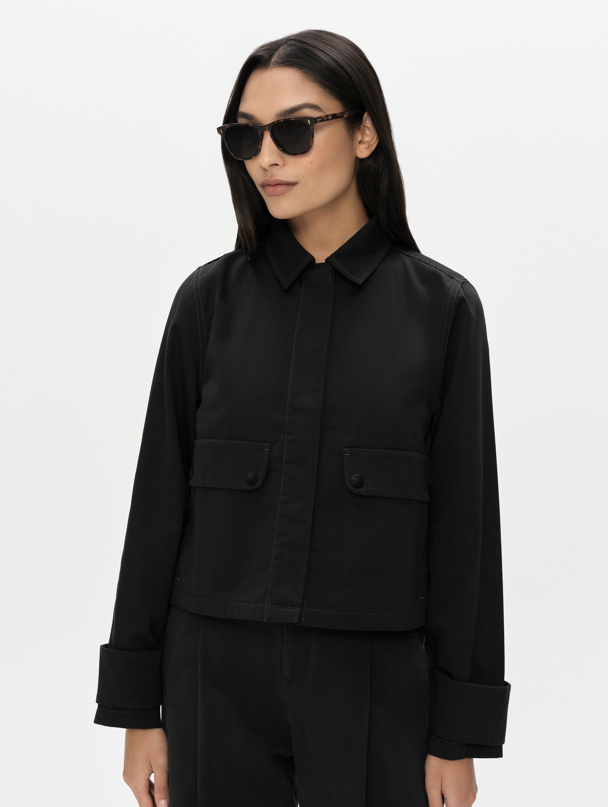 Front, upper-body view of woman wearing the Raven Waxed Cotton Jacket in Onyx Black from AETHER Apparel.