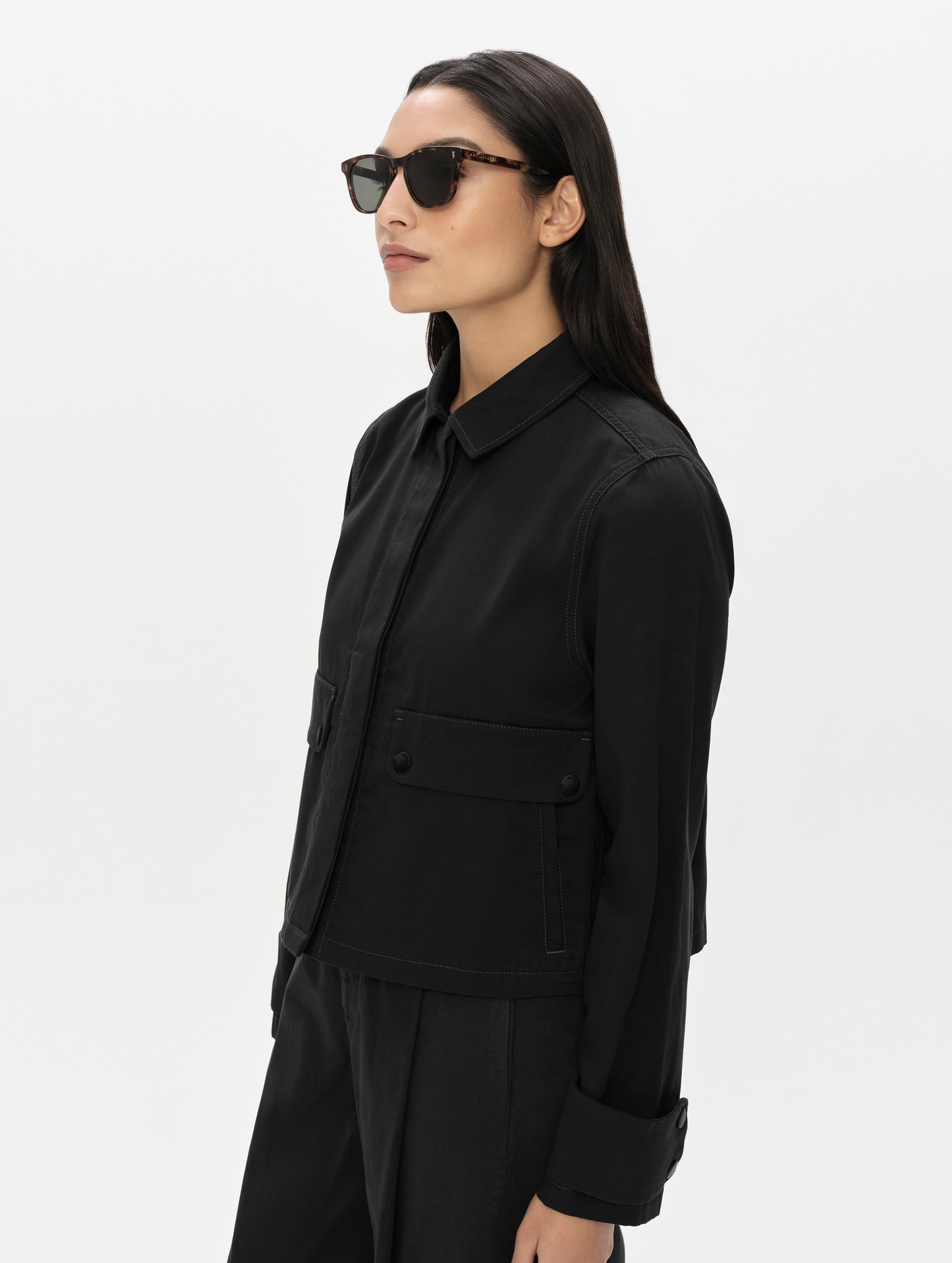 Front, 3/4, upper-body view of woman wearing the Raven Waxed Cotton Jacket in Onyx Black from AETHER Apparel.