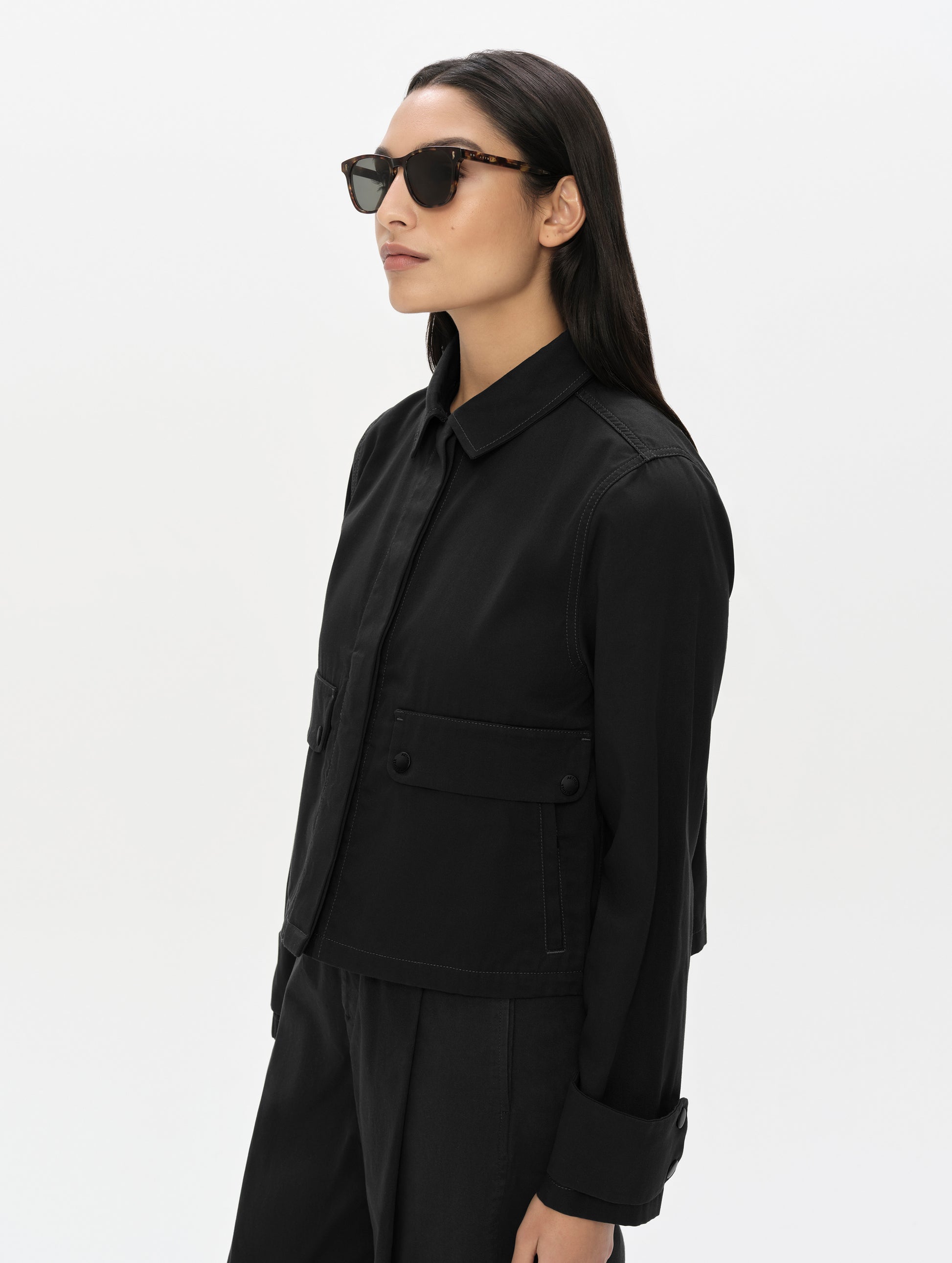 Front, 3/4, upper-body view of woman wearing the Raven Waxed Cotton Jacket in Onyx Black from AETHER Apparel.