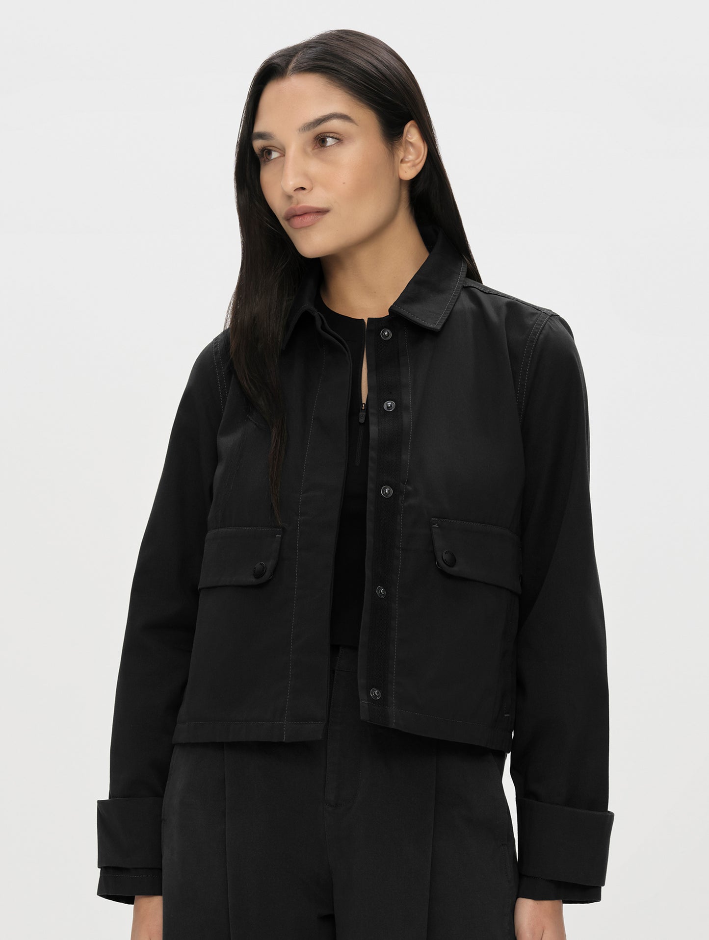 Front, upper-body view of woman wearing the Raven Waxed Cotton Jacket in Onyx Black from AETHER Apparel unsnapped. 
