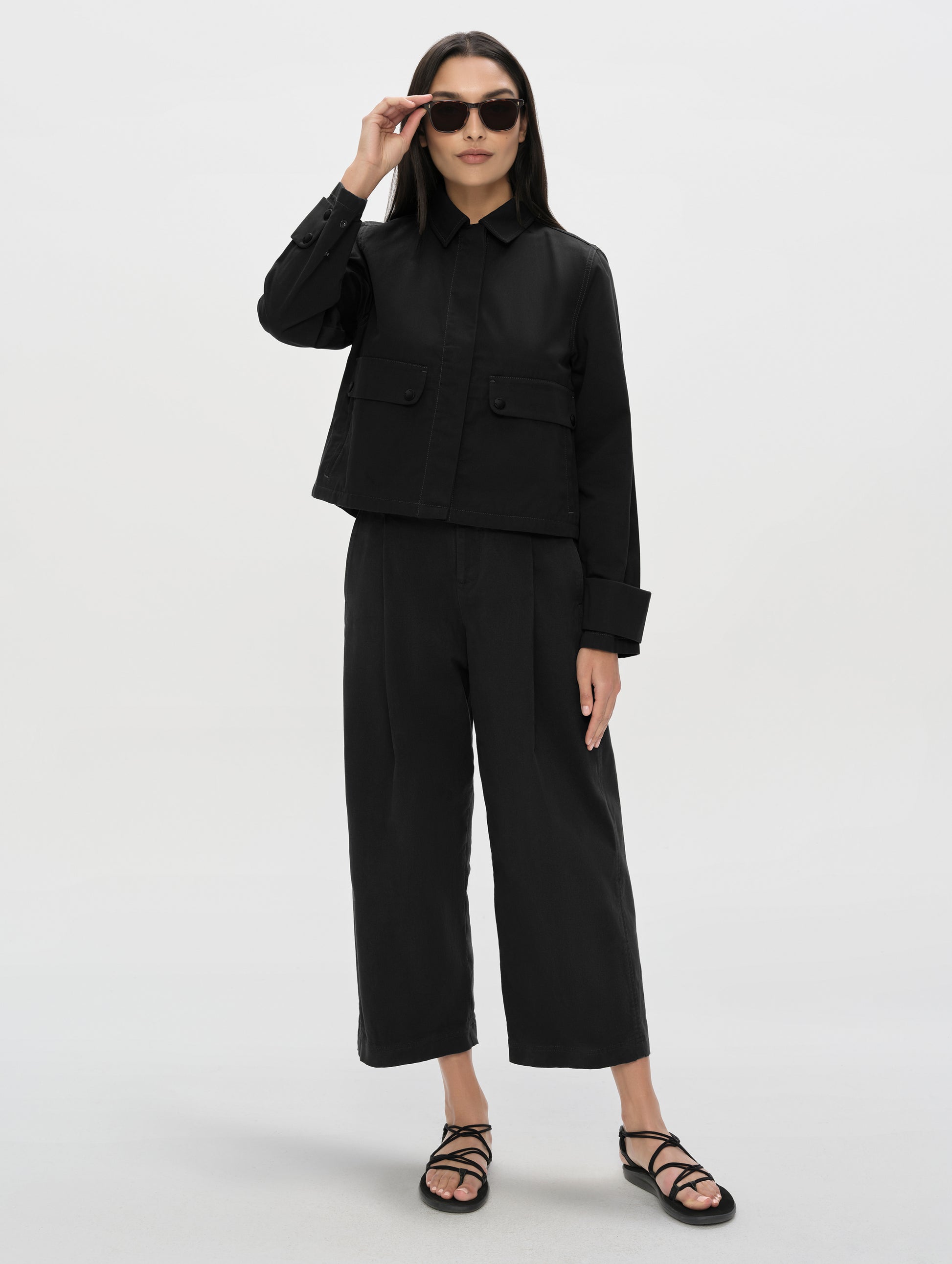 Front, full-body view of woman wearing the Raven Waxed Cotton Jacket in Onyx Black from AETHER Apparel.