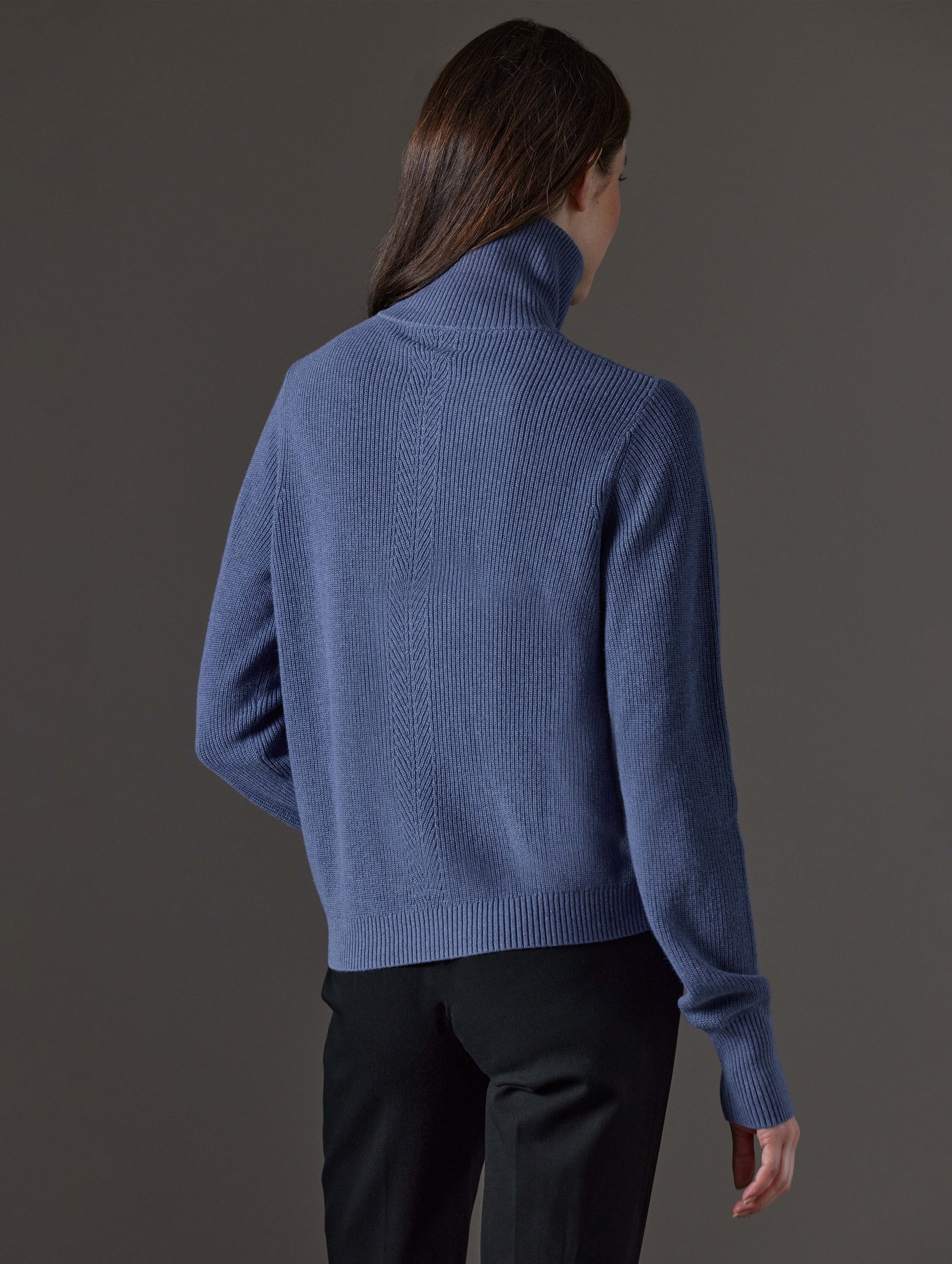 Rear angled view of woman wearing Rhea Full-Zip Sweater in Portal Blue Heather from AETHER Apparel.