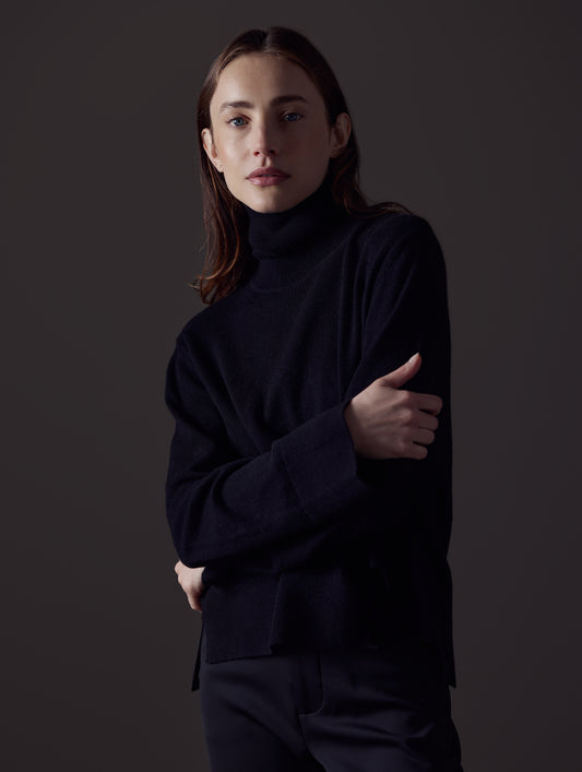 Front angled view of woman with arms crossed wearing Leigh Cashmere Turtleneck Sweater in Onyx Black from AETHER Apparel.
