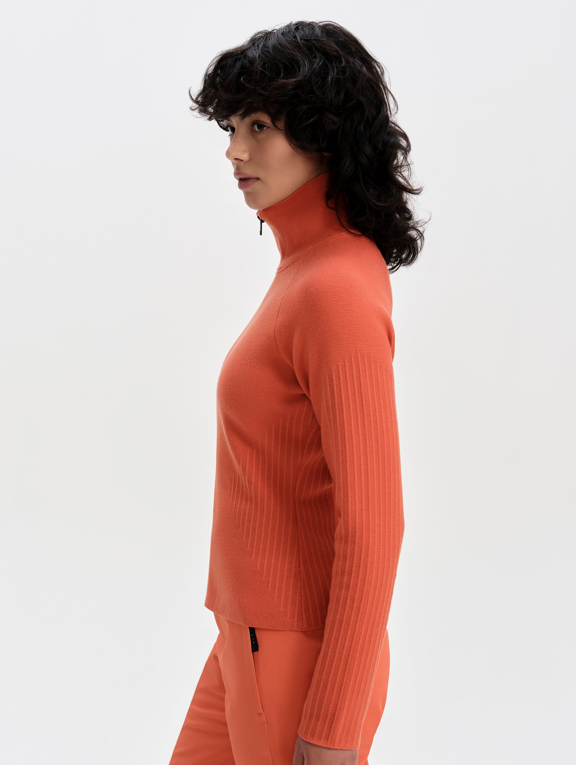 Side profile upper-body view of woman wearing the Riley Full-Zip Sweater 2.0 in Madeira Orange from AETHER Apparel.