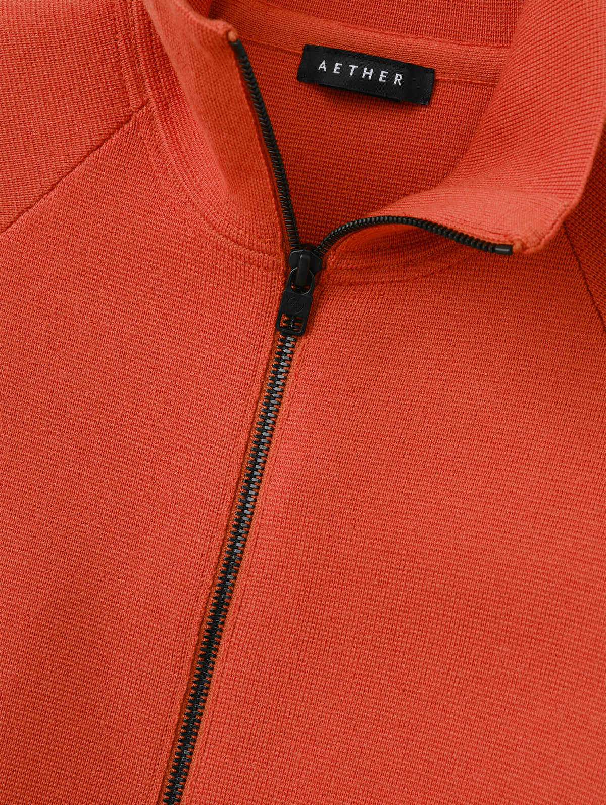 Flat lay view of the center-front zipper on the Riley Full-Zip Sweater 2.0 in Madeira Orange from AETHER Apparel.