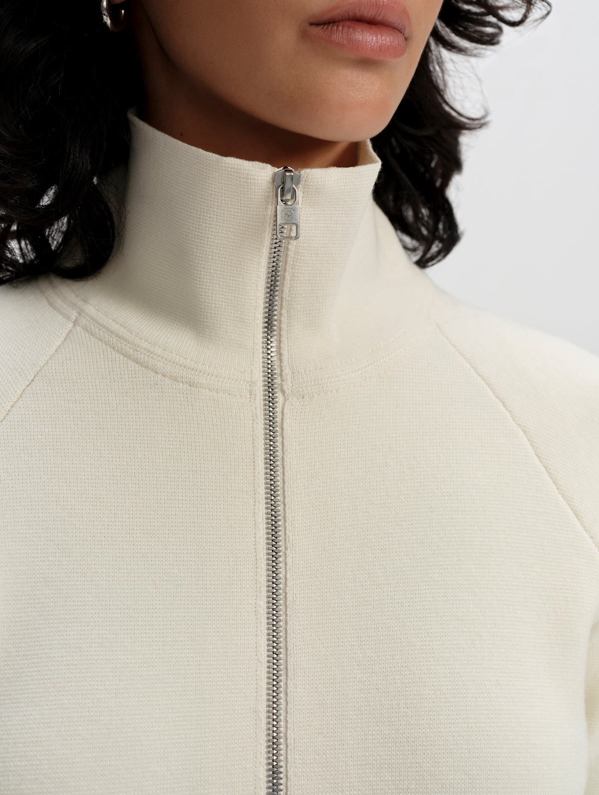 Closeup detailed view of the center-front zipper and collar on the Riley Full-Zip Sweater 2.0 in Winter White from AETHER Apparel.