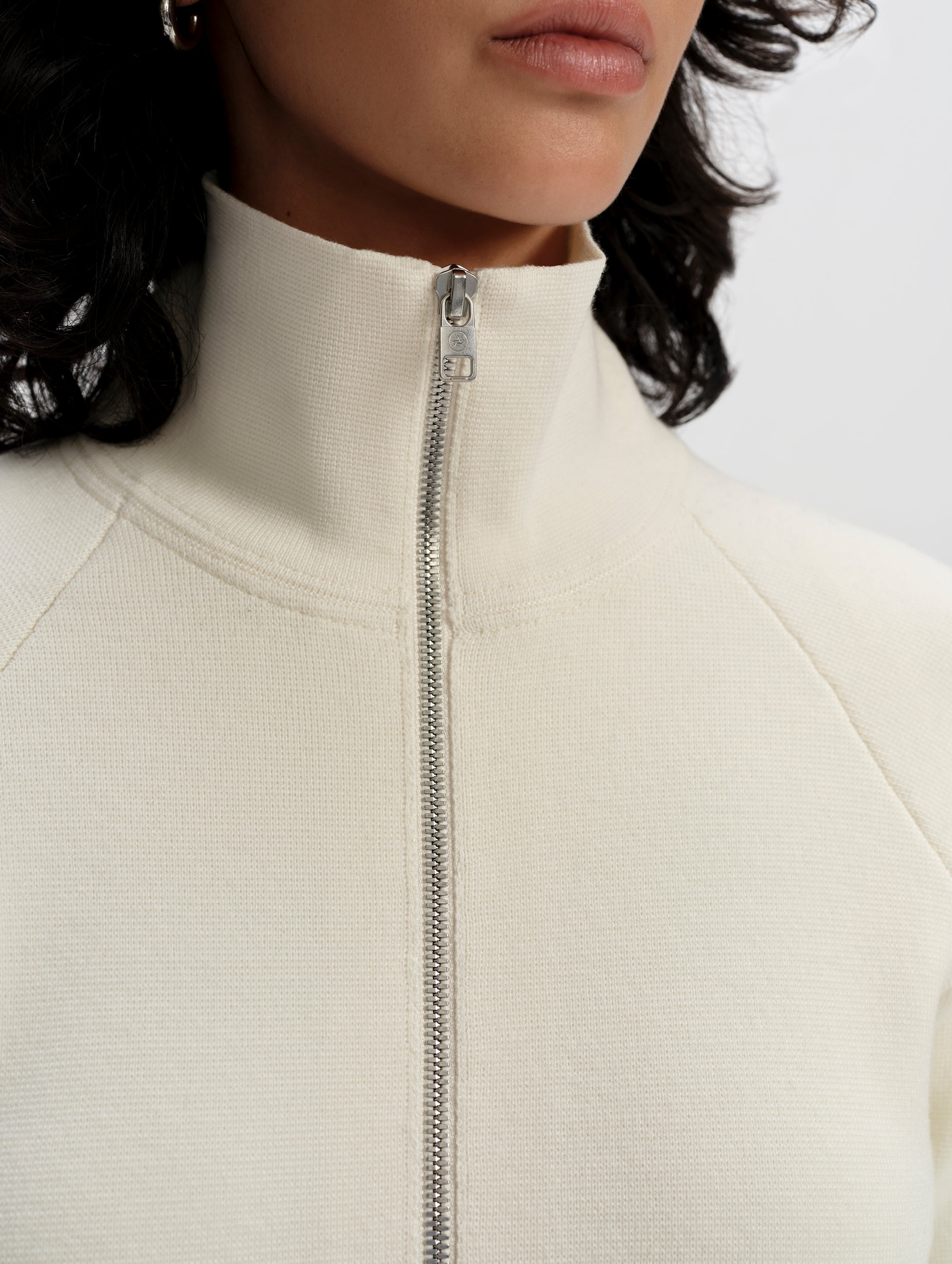 Closeup detailed view of the center-front zipper and collar on the Riley Full-Zip Sweater 2.0 in Winter White from AETHER Apparel.