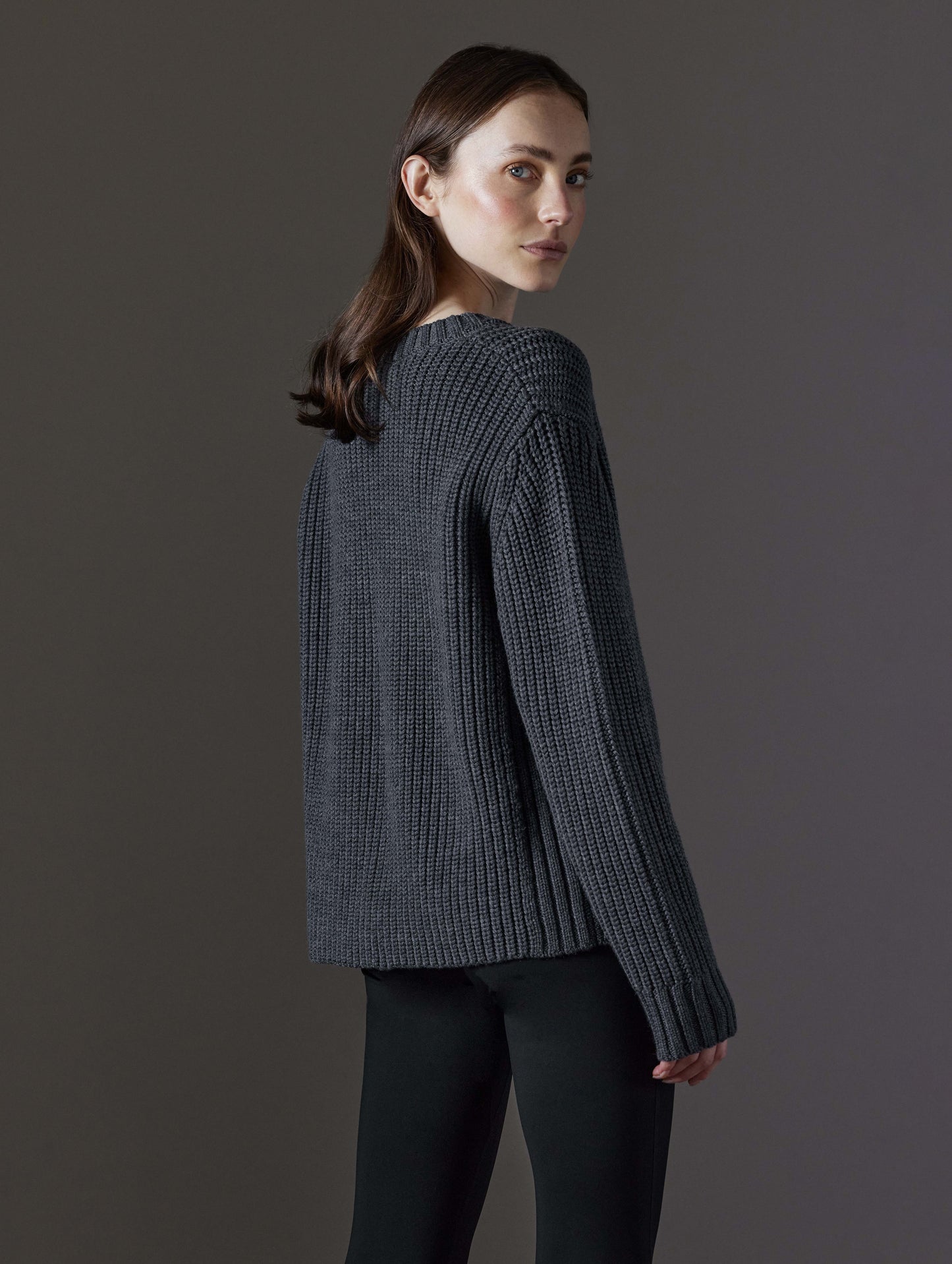 Rear angled view of woman wearing Sherwood Crewneck Sweater in Dark Grey Heather from AETHER Apparel.