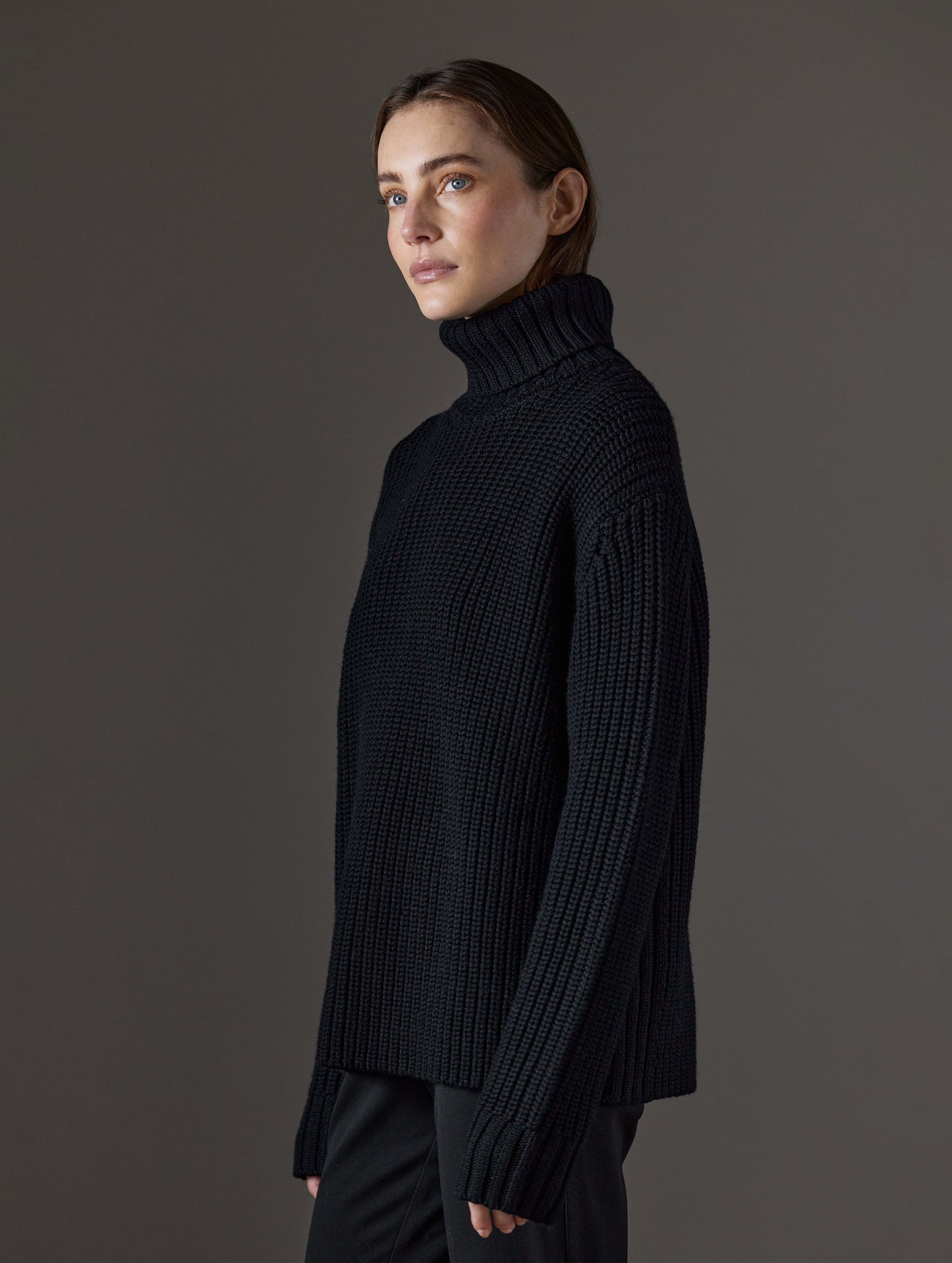 Side profile view of woman wearing Sherwood Turtleneck Sweater in Onyx Black from AETHER Apparel.