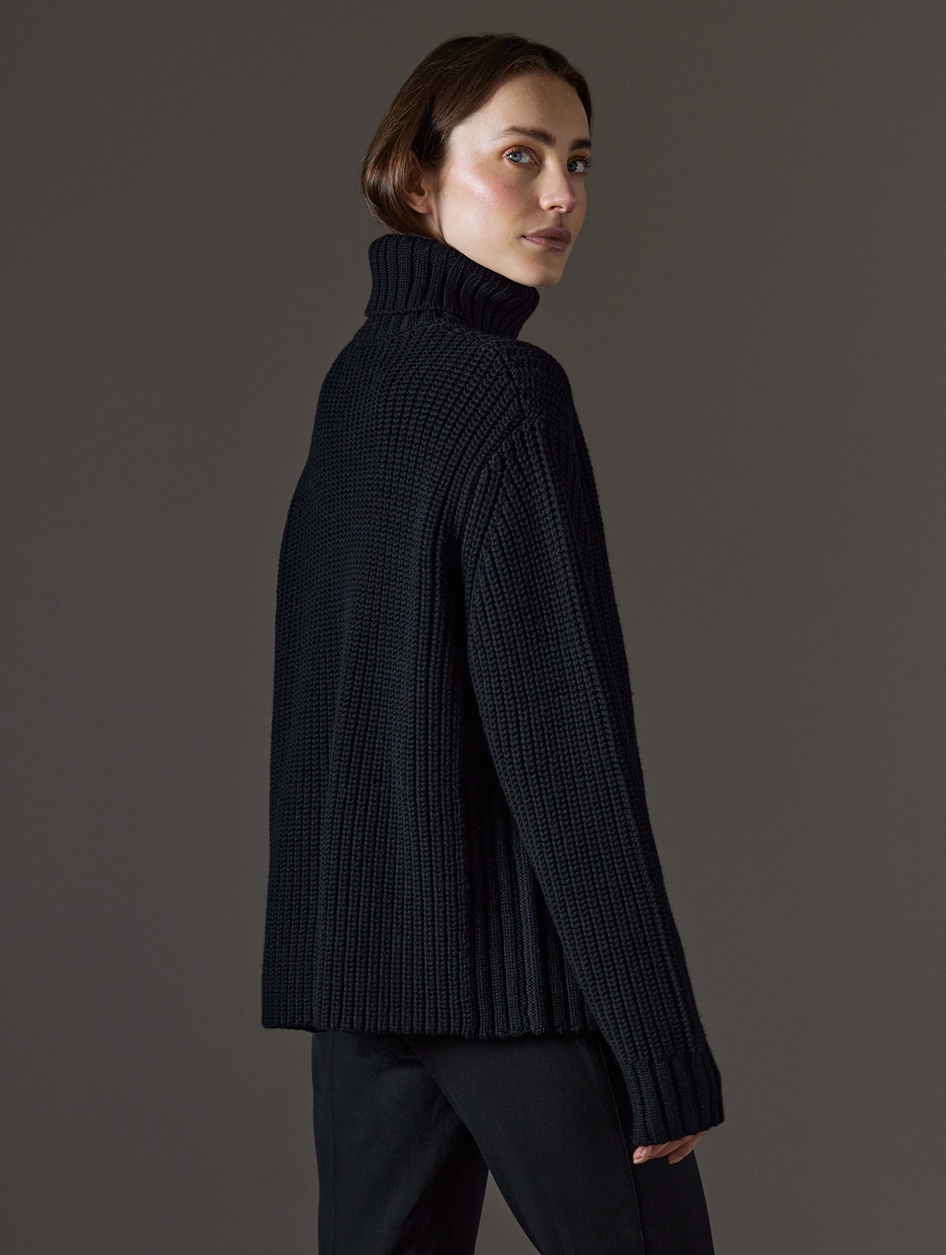 Rear angled view of woman wearing Sherwood Turtleneck Sweater in Onyx Black from AETHER Apparel.