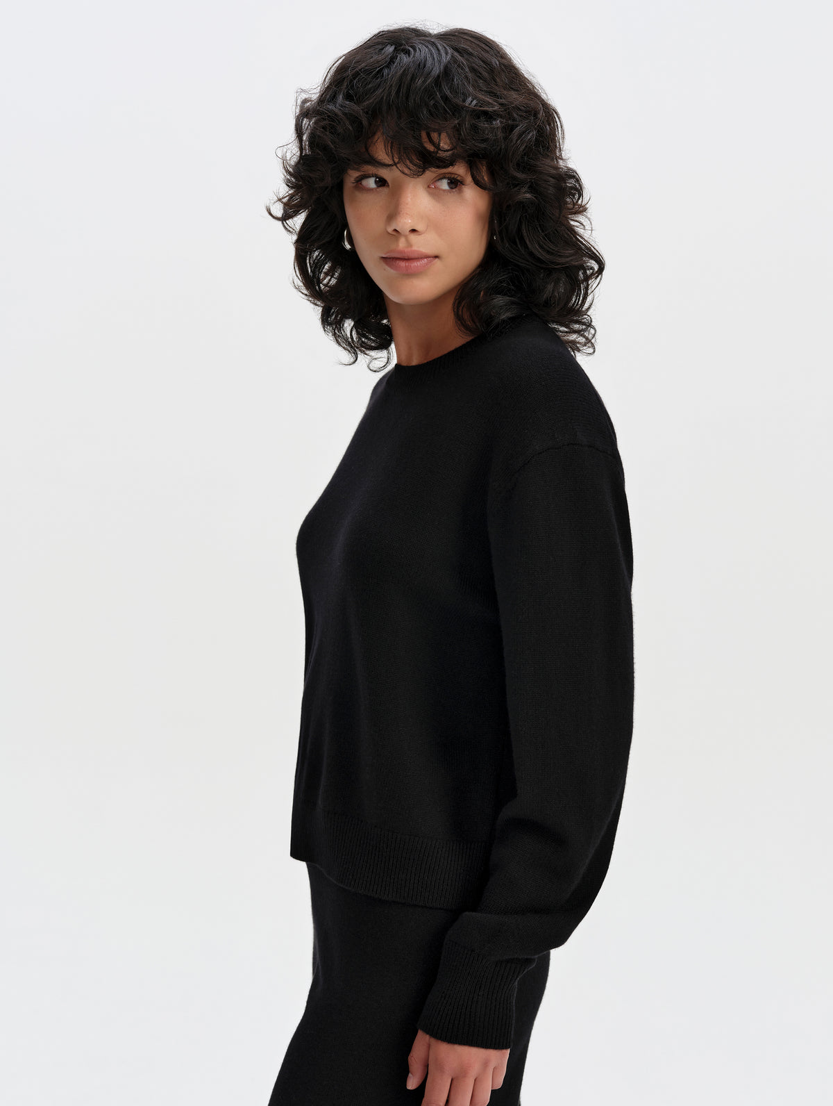 Side profile upper-body view of woman wearing the Solace Cashmere Sweater in Onyx Black from AETHER Apparel.