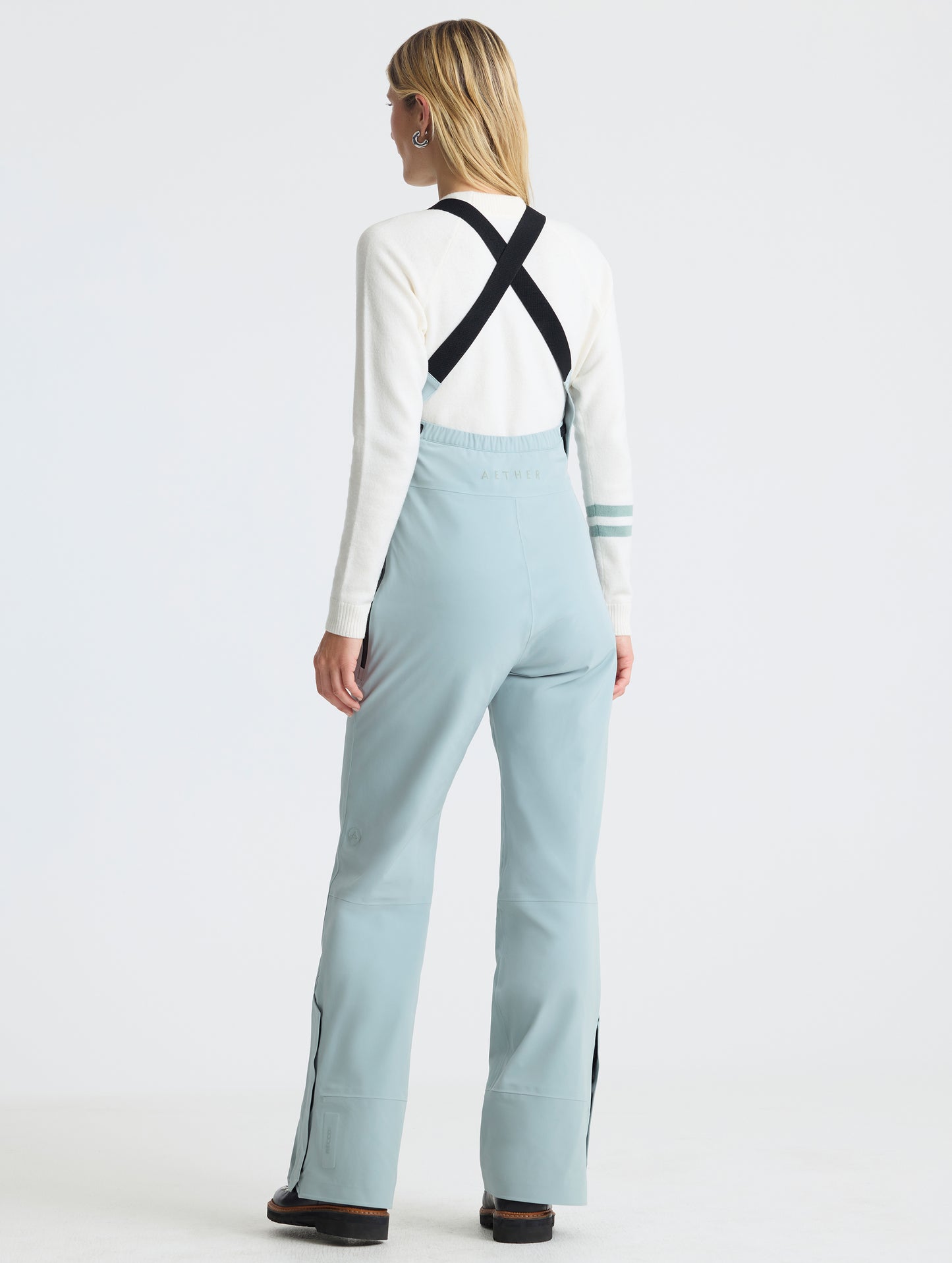 Rear angled full-body view of woman wearing the Sophia Insulated Snow Bib in Jadewood Green from AETHER Apparel.