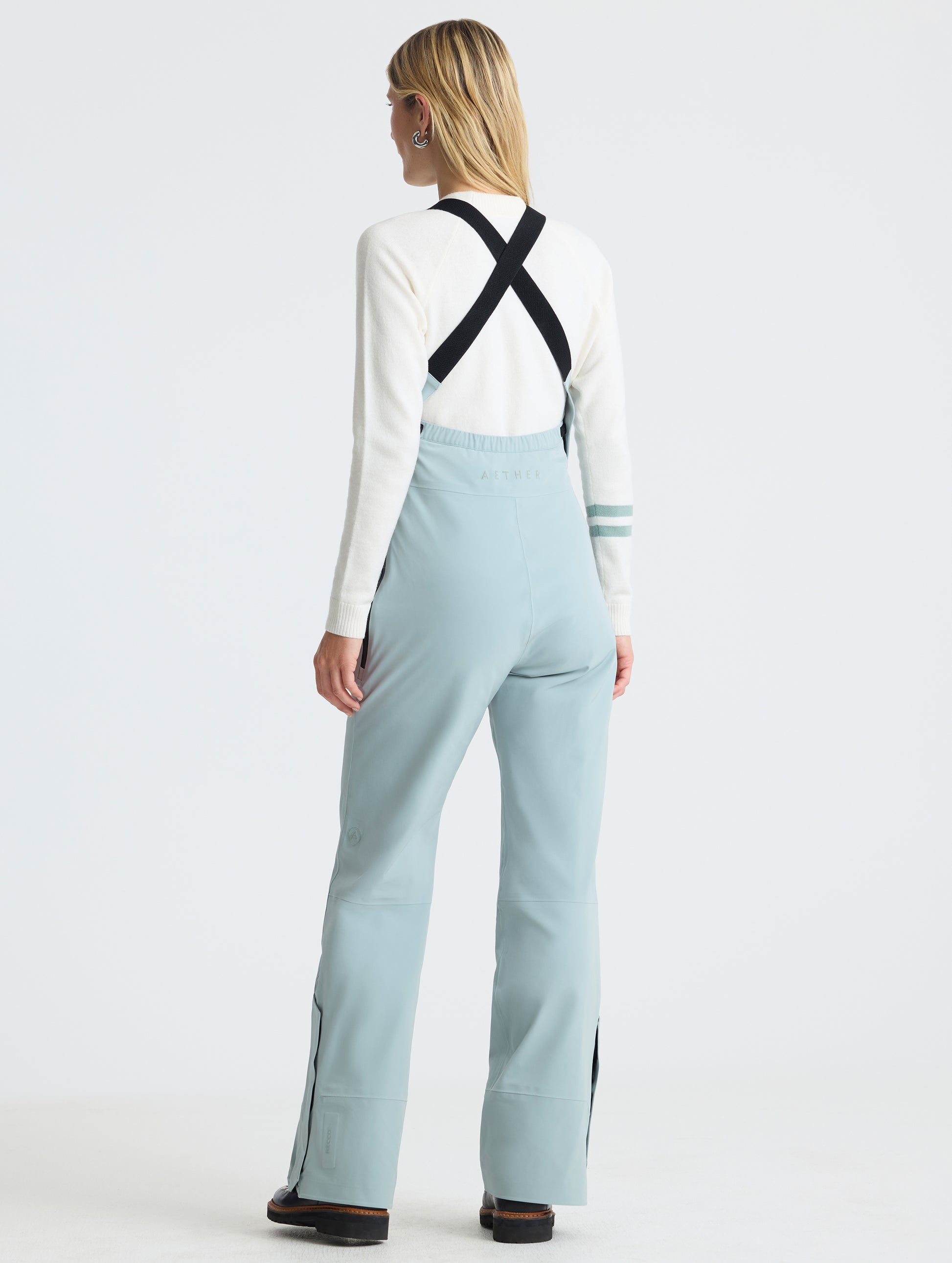 Rear angled full-body view of woman wearing the Sophia Insulated Snow Bib in Jadewood Green from AETHER Apparel.