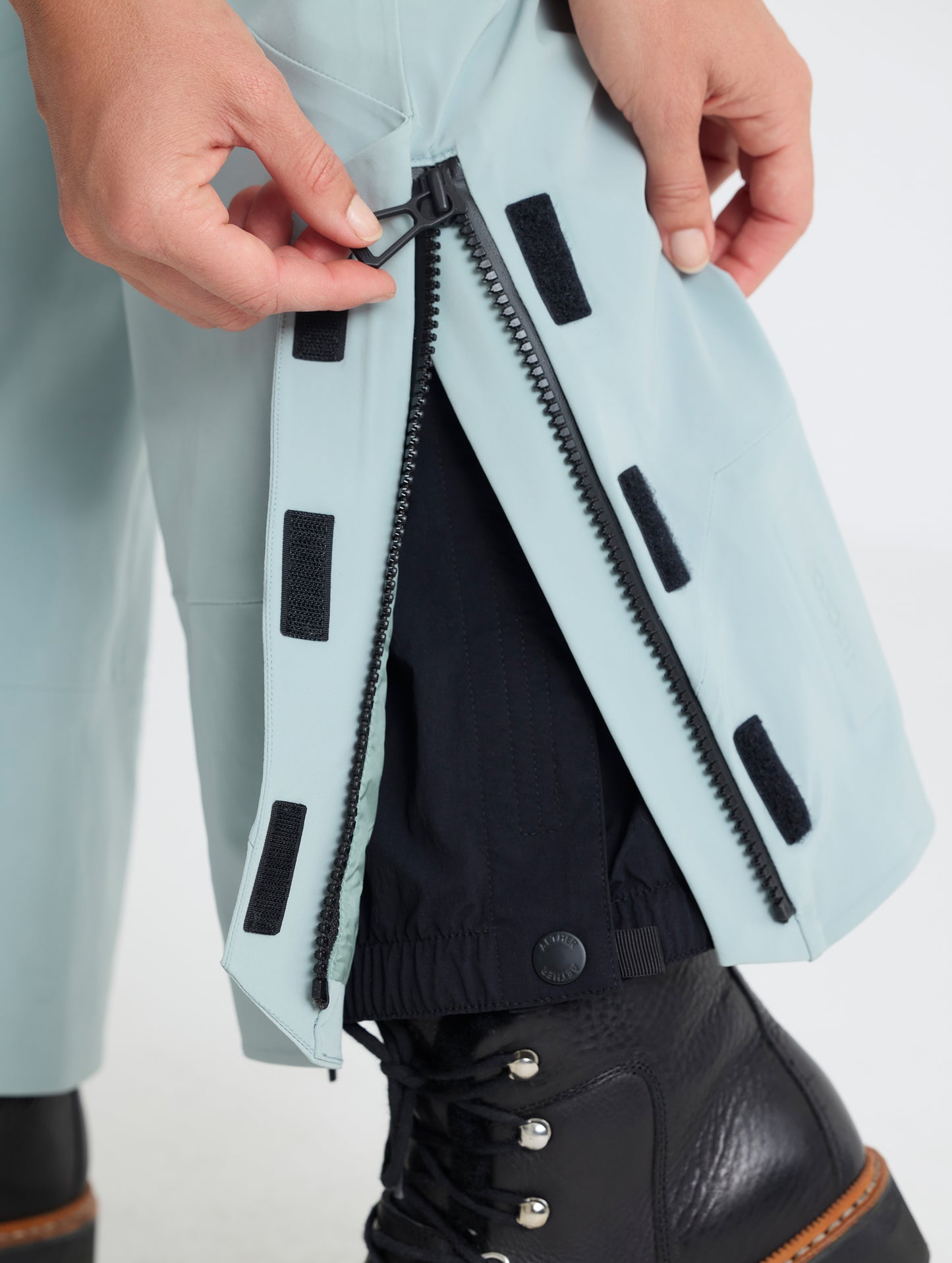 Closeup detailed view of the zipper and Velcro-secured adjustable leg cuff openings on the Sophia Insulated Snow Bib in Jadewood Green from AETHER Apparel.