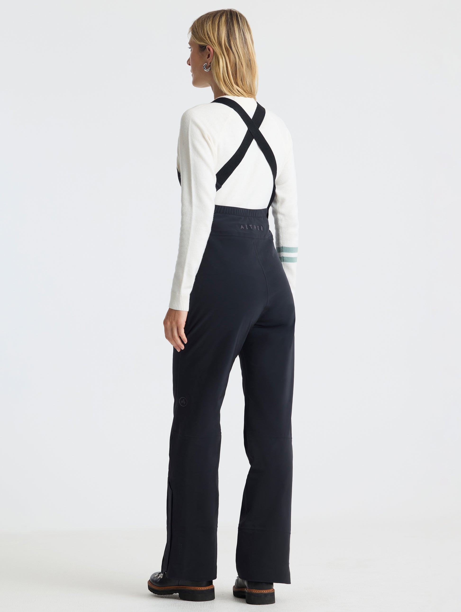 Rear angled full-body view of woman wearing the Sophia Insulated Snow Bib in Onyx Black from AETHER Apparel.